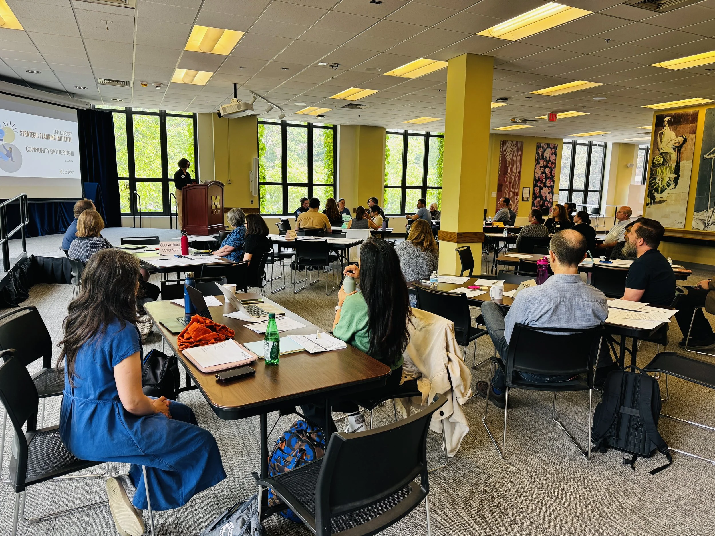 A group gathering sitting in multiple tables with a speaker at a podium