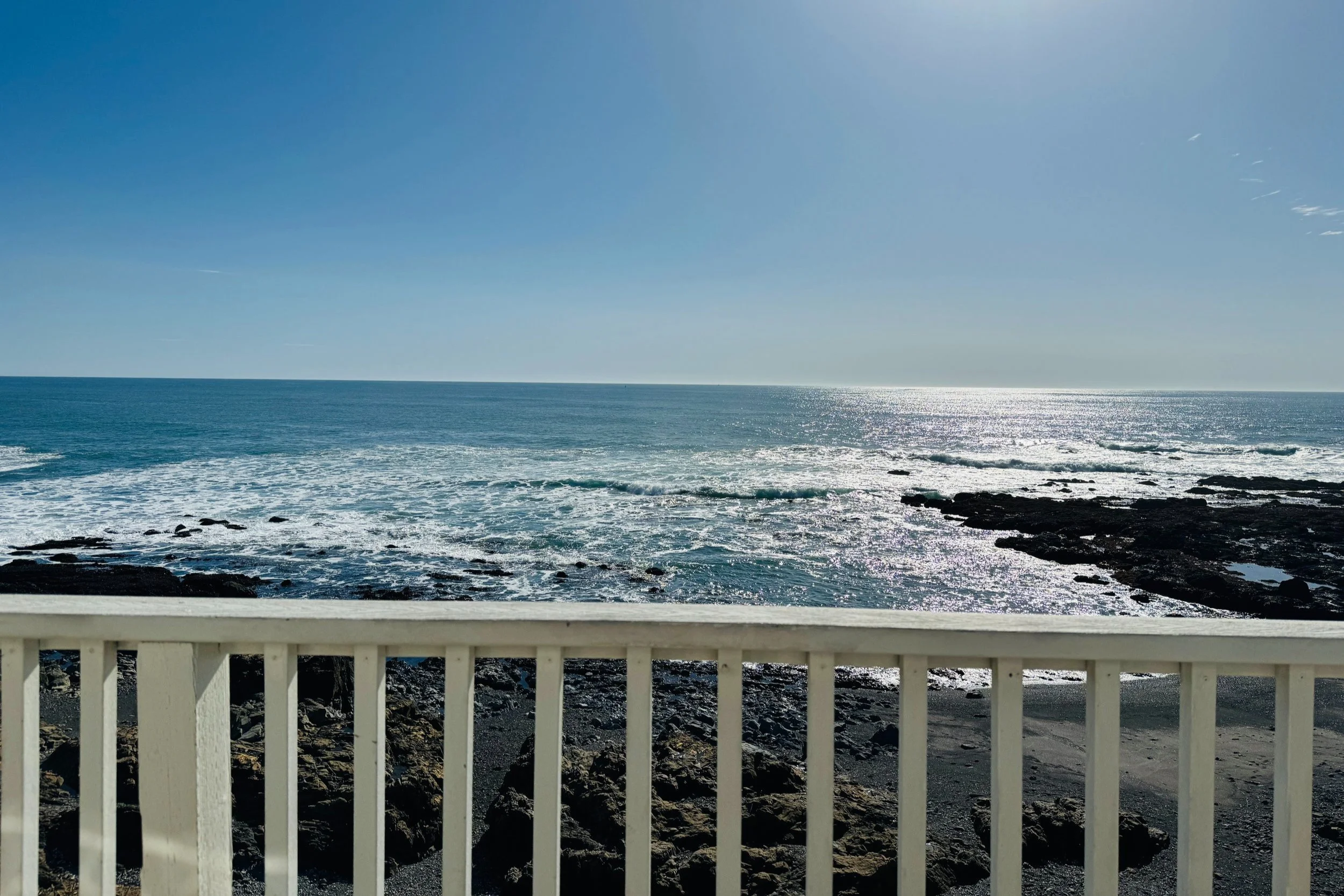 A serene view of the ocean glittering under the sunlight, captured from behind a white railing, showcasing nature’s tranquility and beauty.