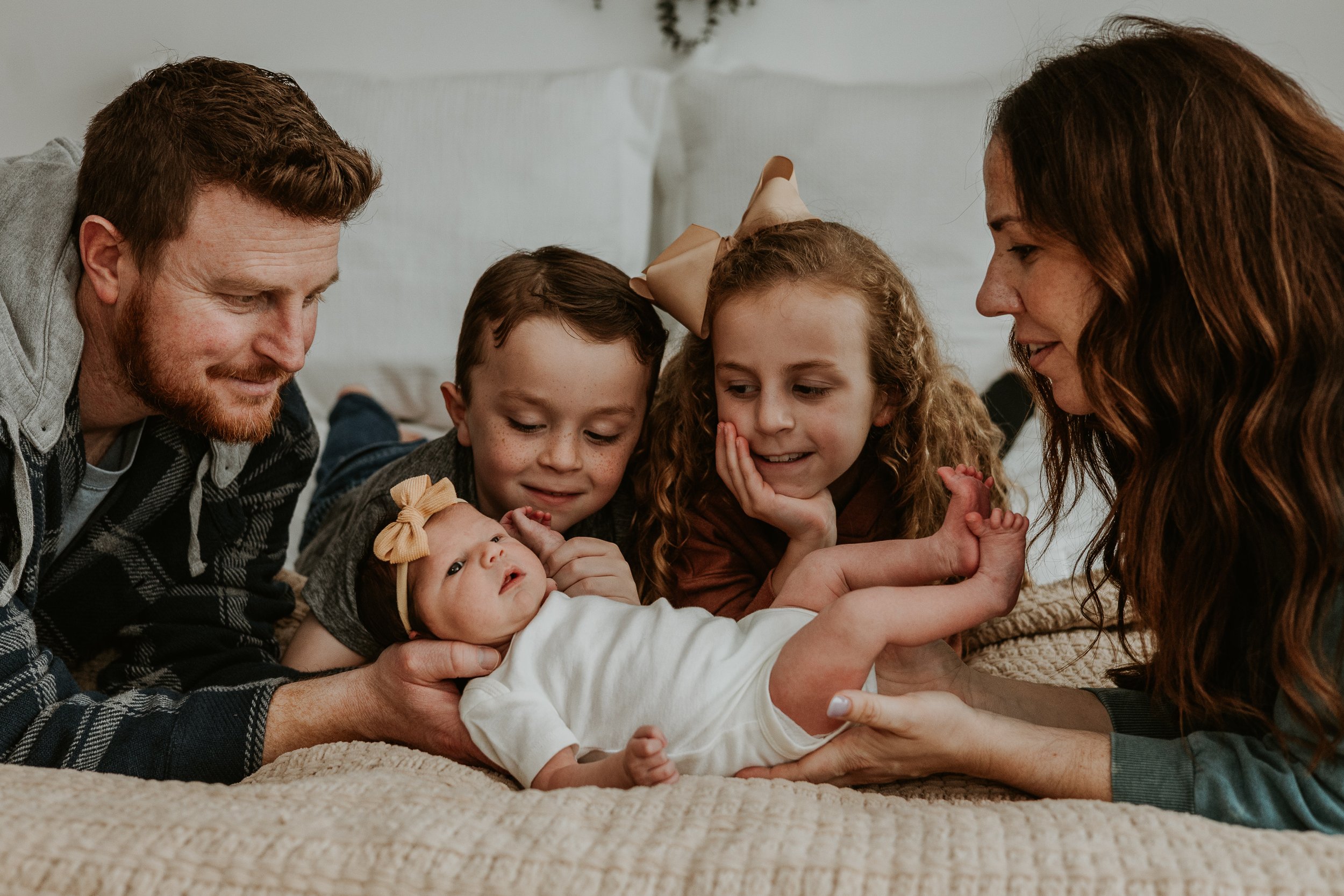 Everyone wants to hold the baby - mom at baby's feet, dad supporting baby's head, as brother and sister look on waiting for their turn next.
