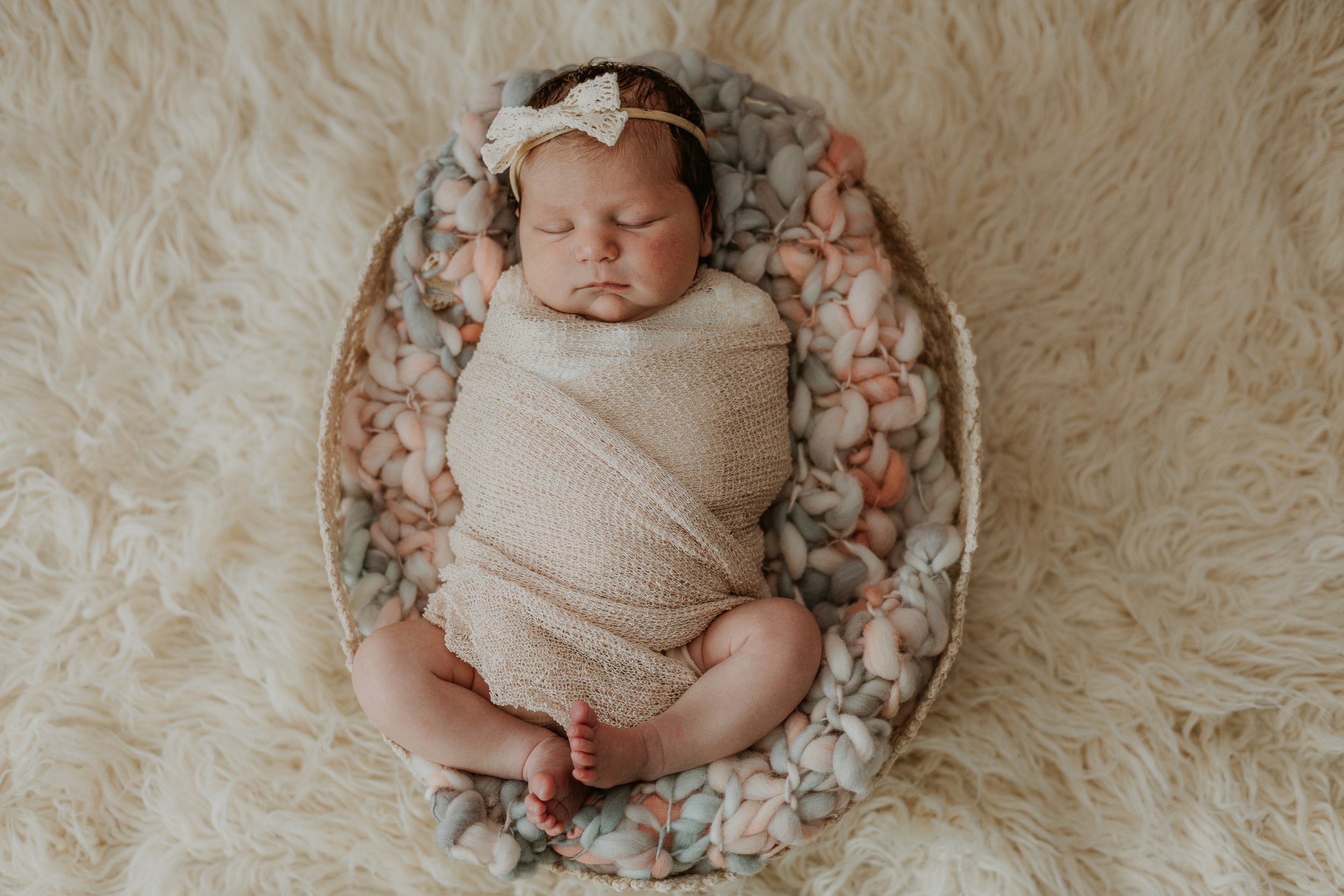 An overhead view of a posed newborn swaddled atop fluffy blankets in a woven basket.