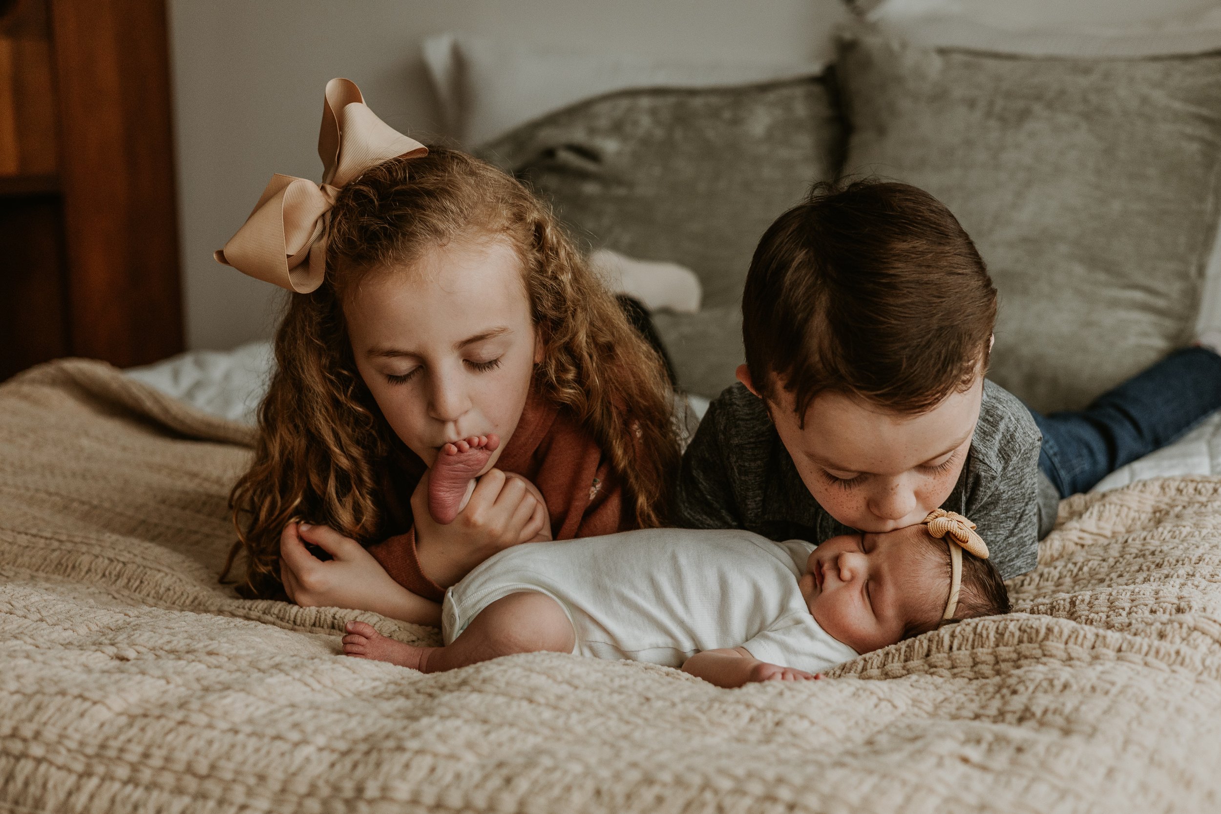 Big brother and big sister lay kisses on their baby sister's head and foot during a photoshoot in Bloomington Illinois.
