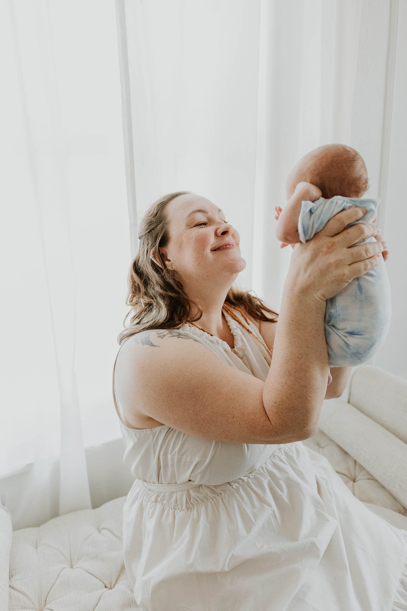 A mother admires her baby, lifting her up to see her face during their newborn photography session.