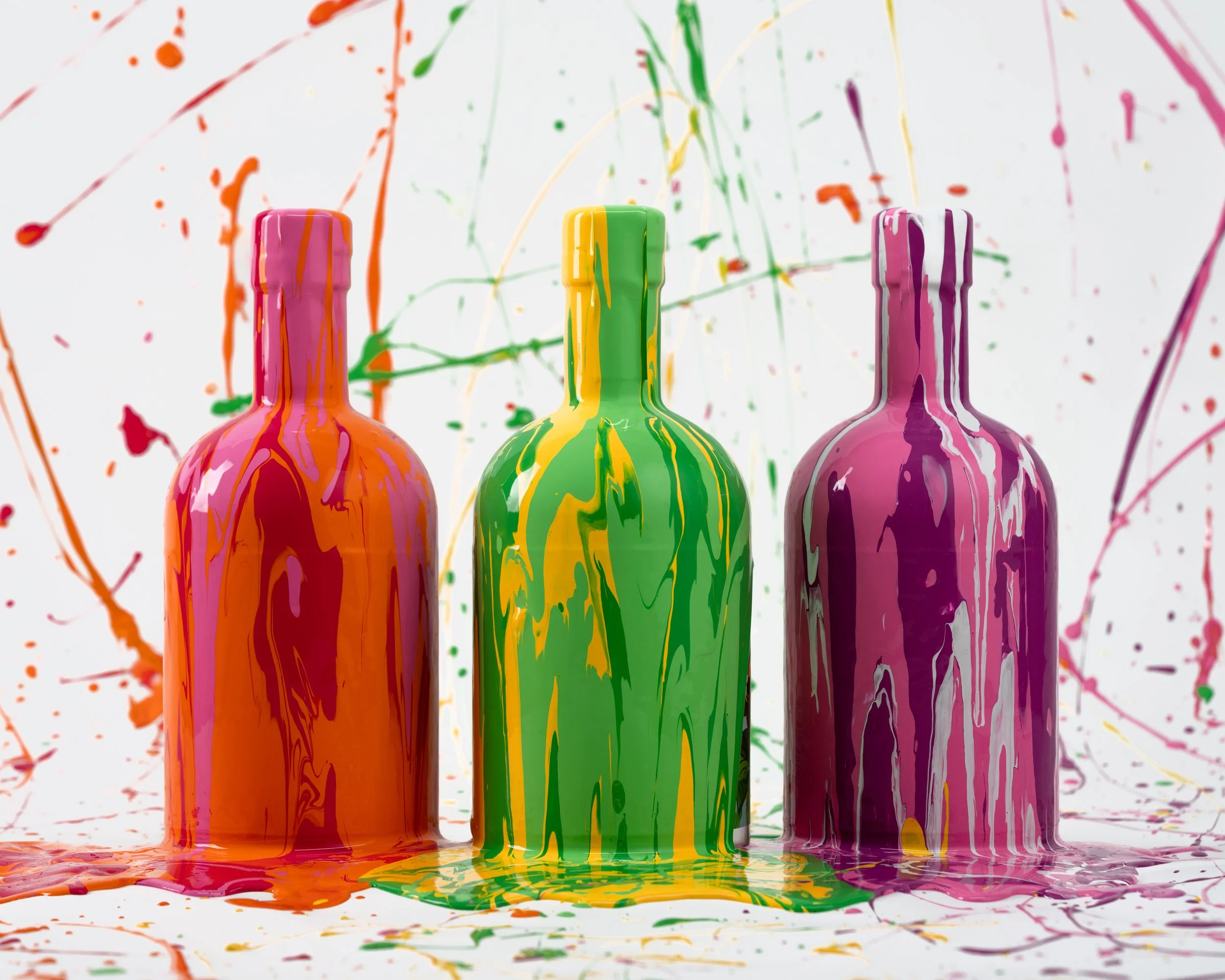 Three bottles covered in splattered paint in orange, green, and purple, with a matching splattered paint background.