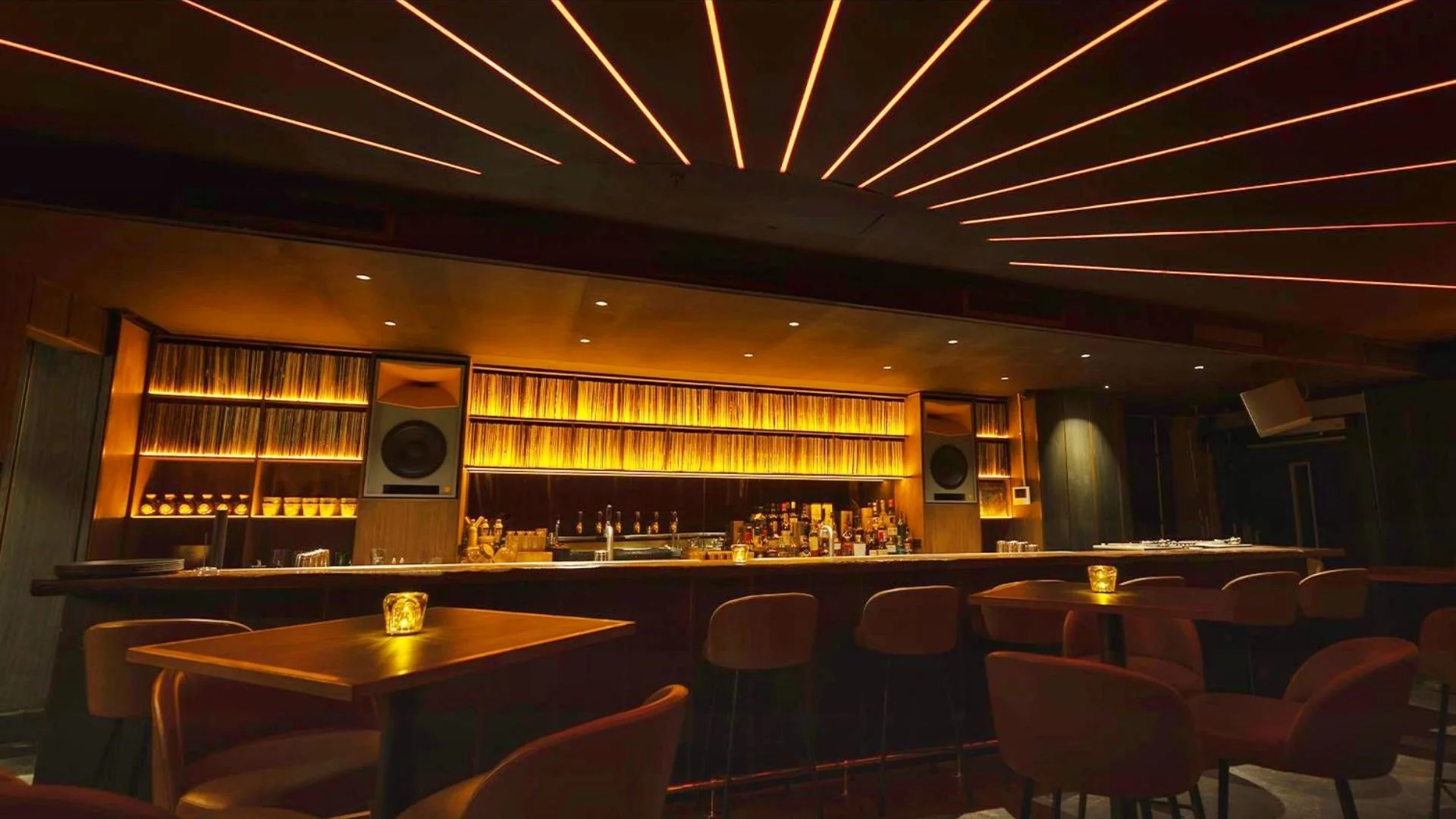 A beautiful cocktail bar with a modern design, featuring a wooden bar counter, shelves filled with bottles, ambient lighting, and a decorative ceiling with orange neon lines.