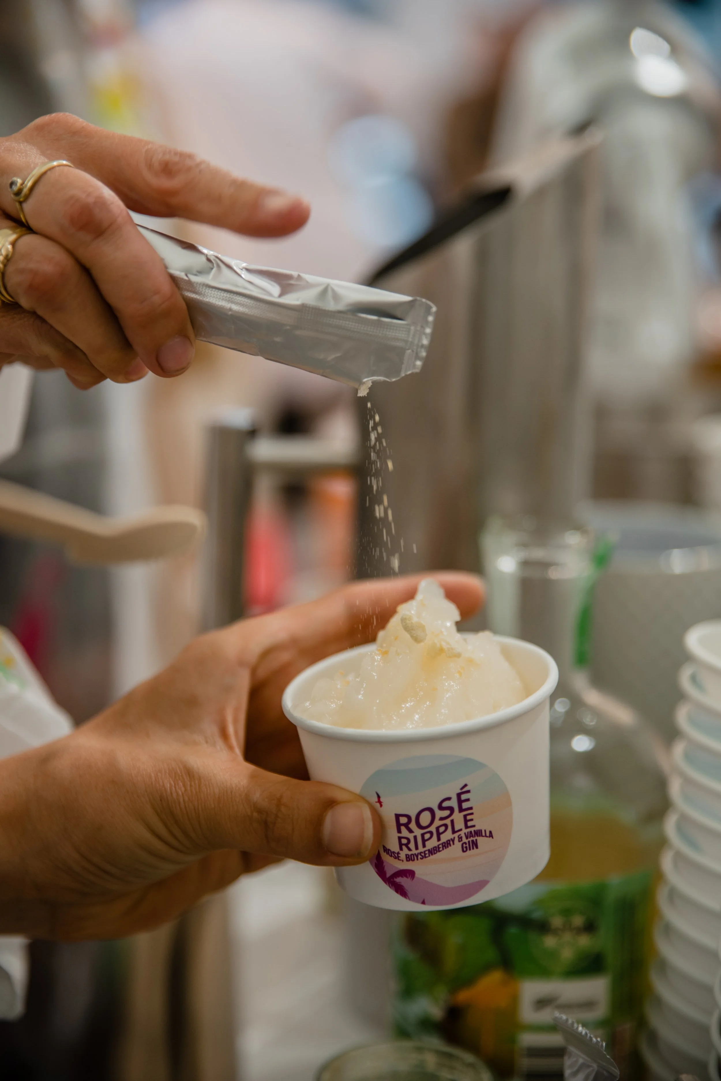 A person sprinkling sugar onto a cup of frozen dessert or ice cream.