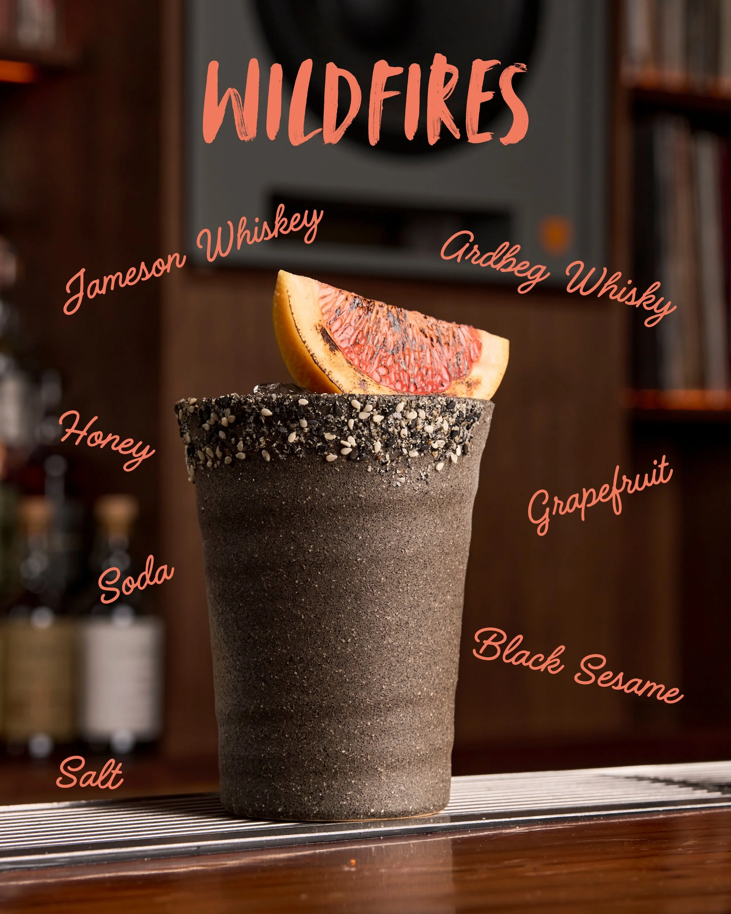 A cocktail glass with a black sesame rim and a slice of grapefruit on top, with various words related to whiskey and cocktail ingredients overlaid on the image, including 'WILDFIRE', 'Jameson Whiskey', 'Glenbeg Whiskey', 'Honey', 'Grapefruit', 'Soda'