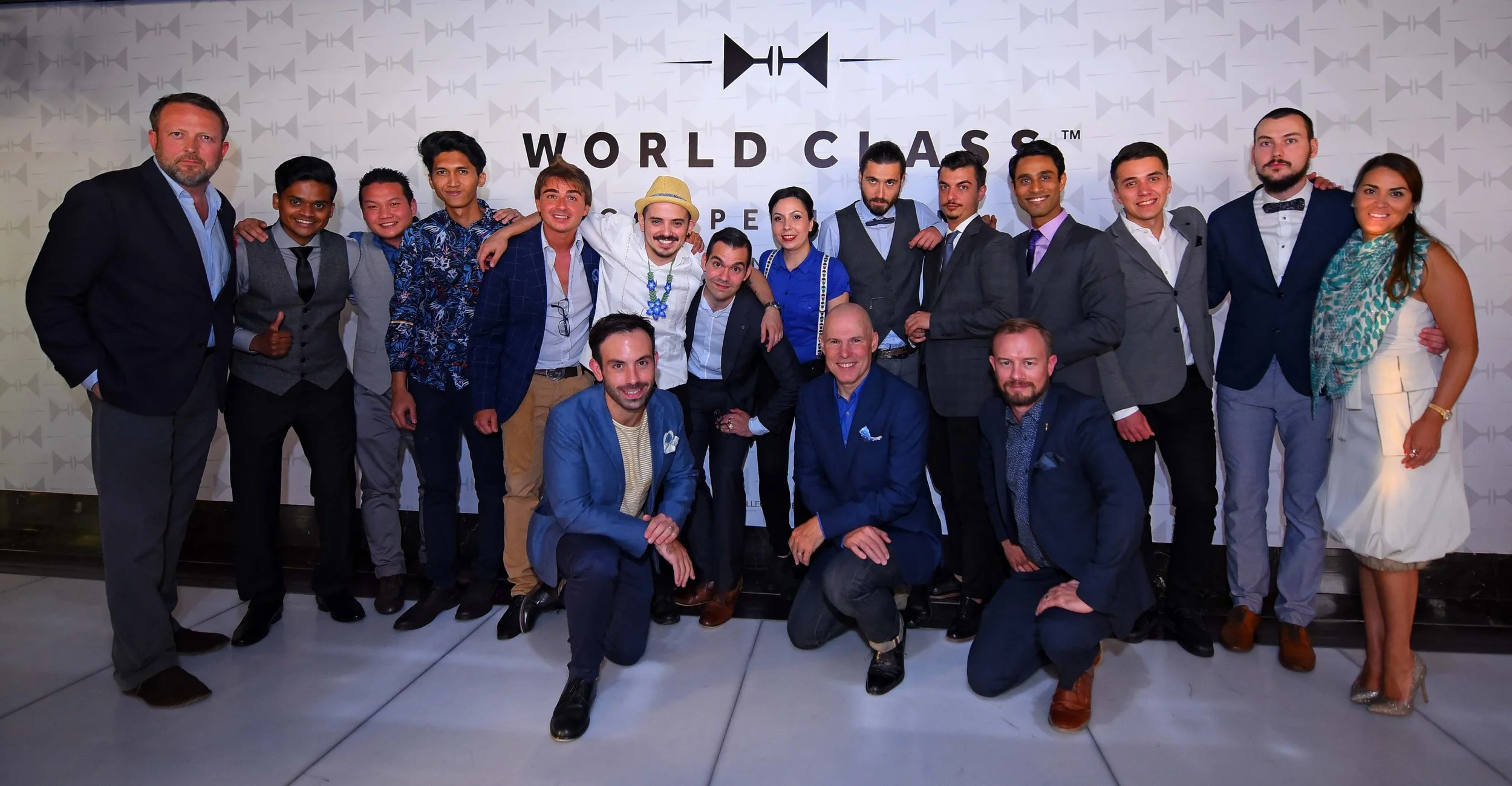 Group of diverse people dressed in formal attire at a decorated event space with a backdrop that reads 'World Class' and features a logo.