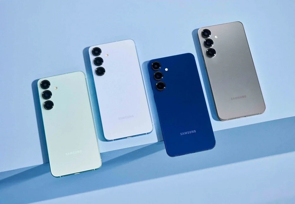 Quatro Samsung Galaxy S25 de costas, em verde-claro, branco, azul-escuro e cinzento, encostados a uma parede azul