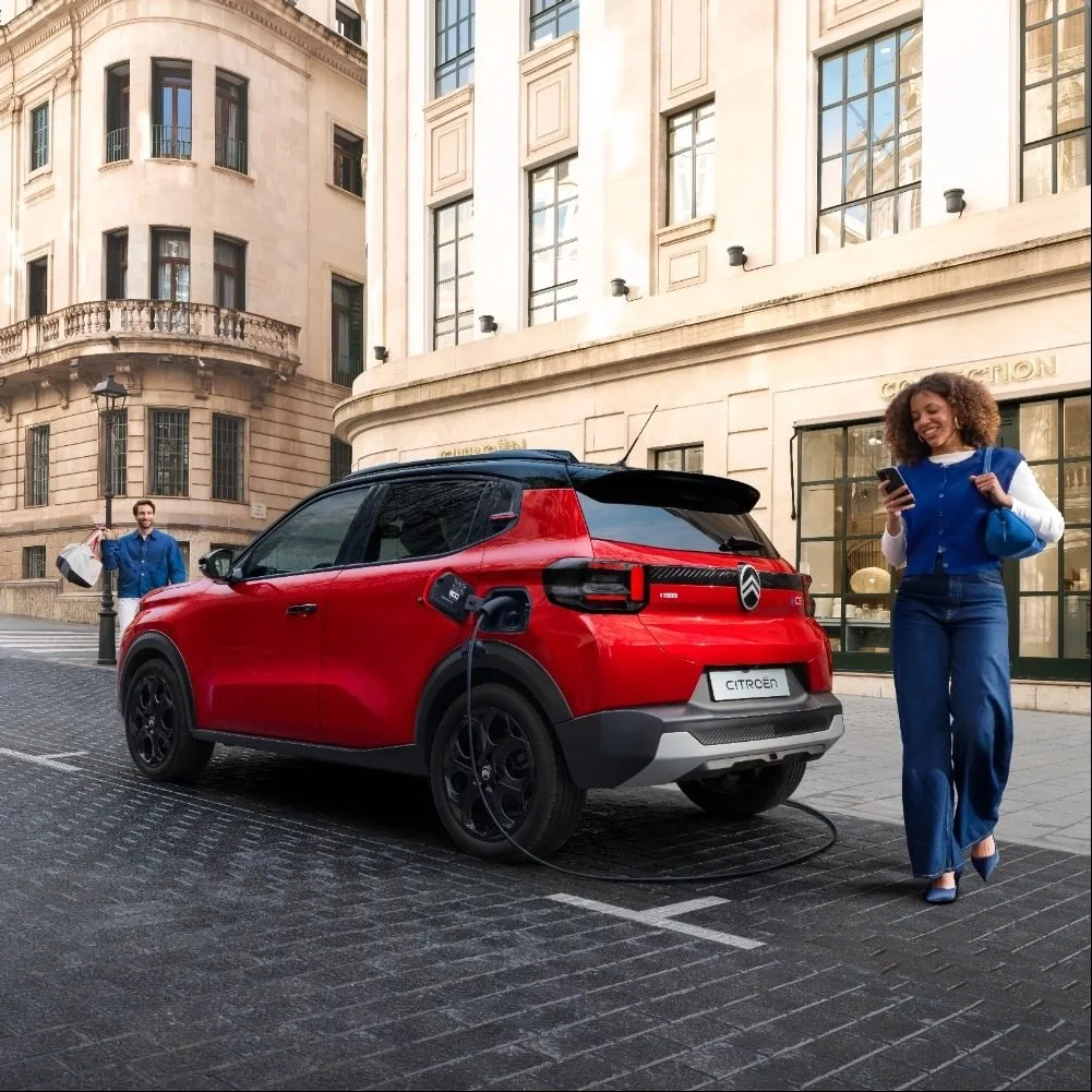 Citroën ë-C3 vermelho a carregar na rua, com uma mulher ao lado a olhar para o telemóvel