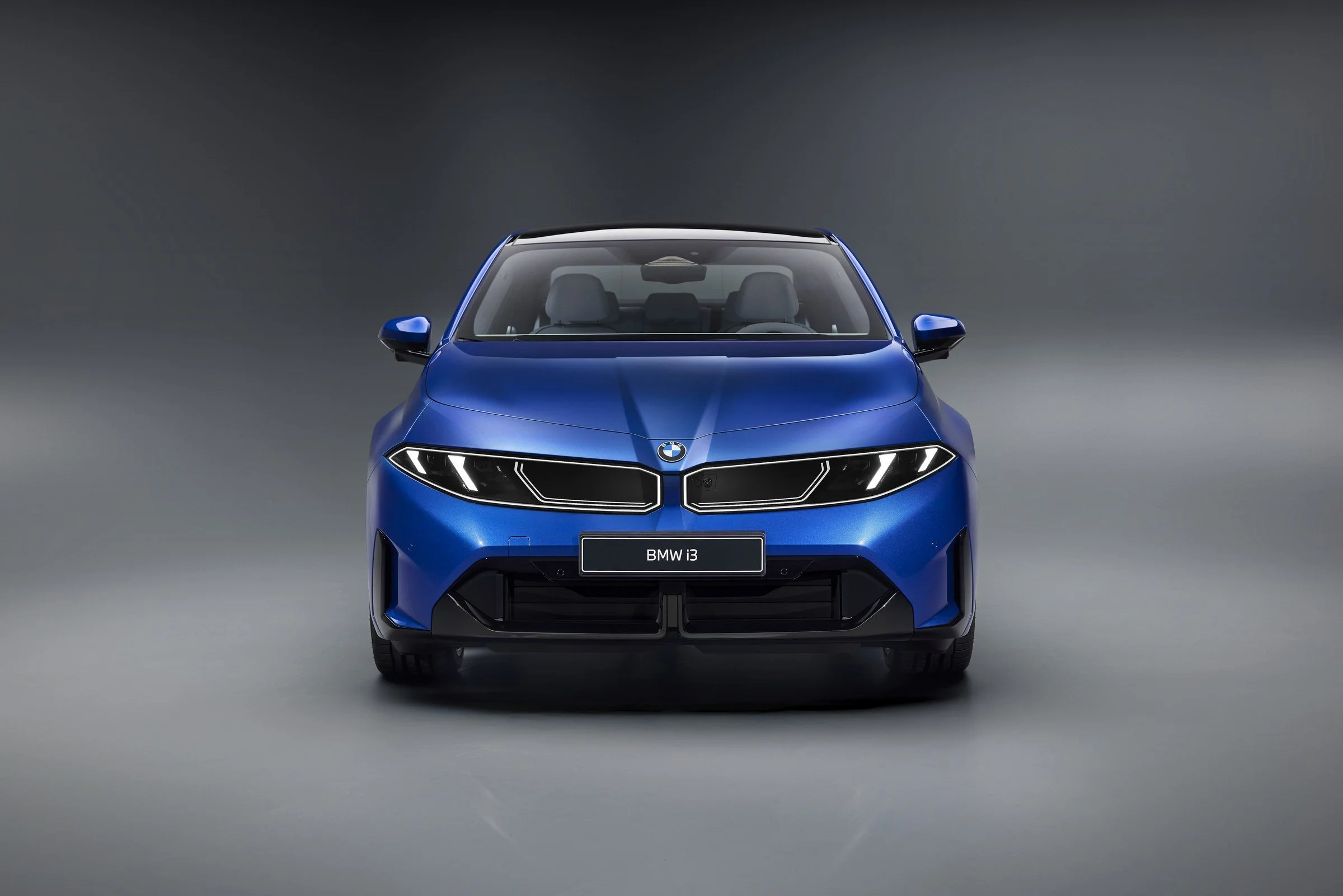 Frente do novo BMW i3 azul num estúdio cinzento claro, com a nova grelha iluminada e os faróis finos