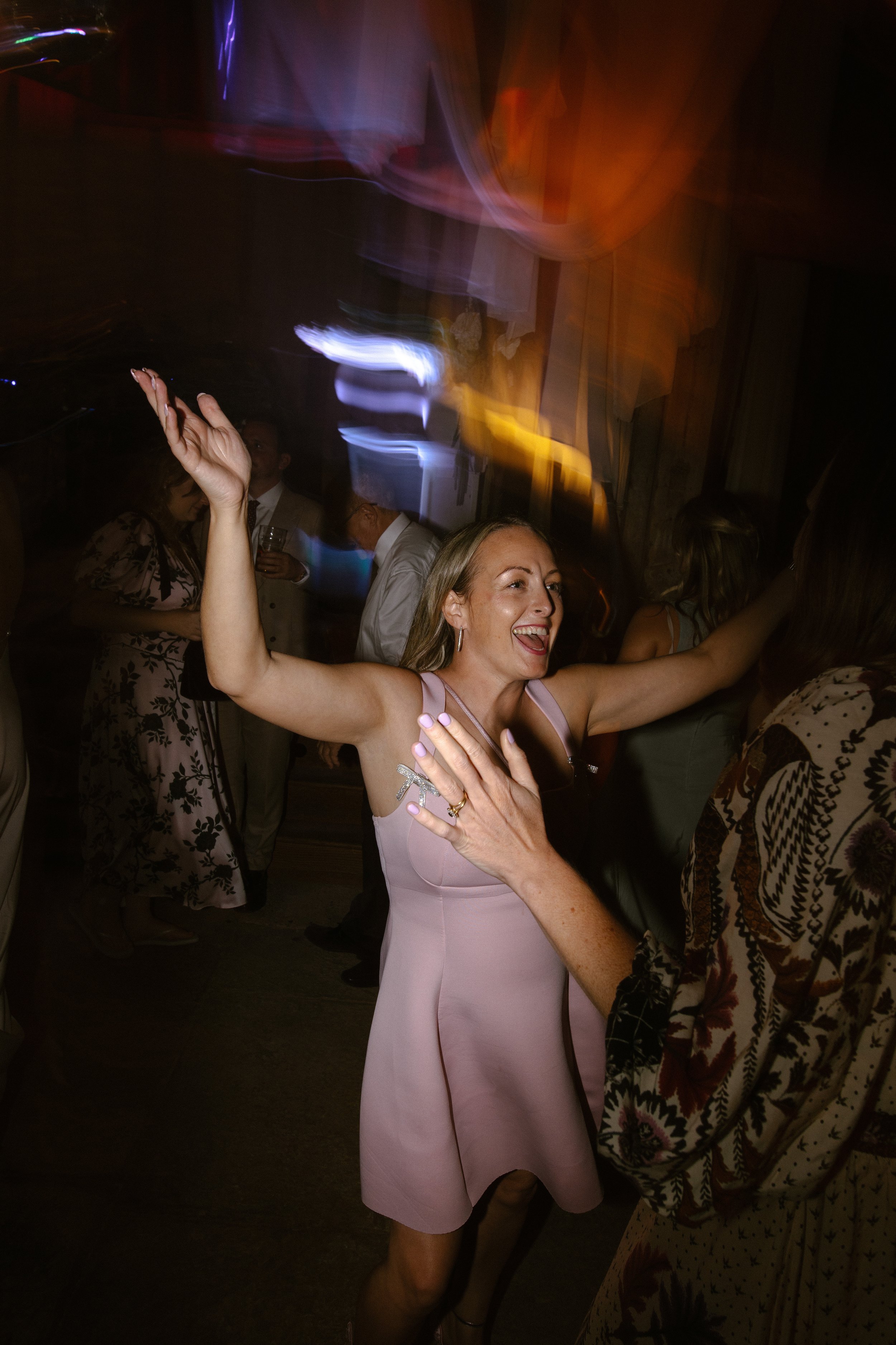 A woman smiling and dancing with her arms raised at a lively party or celebration event.