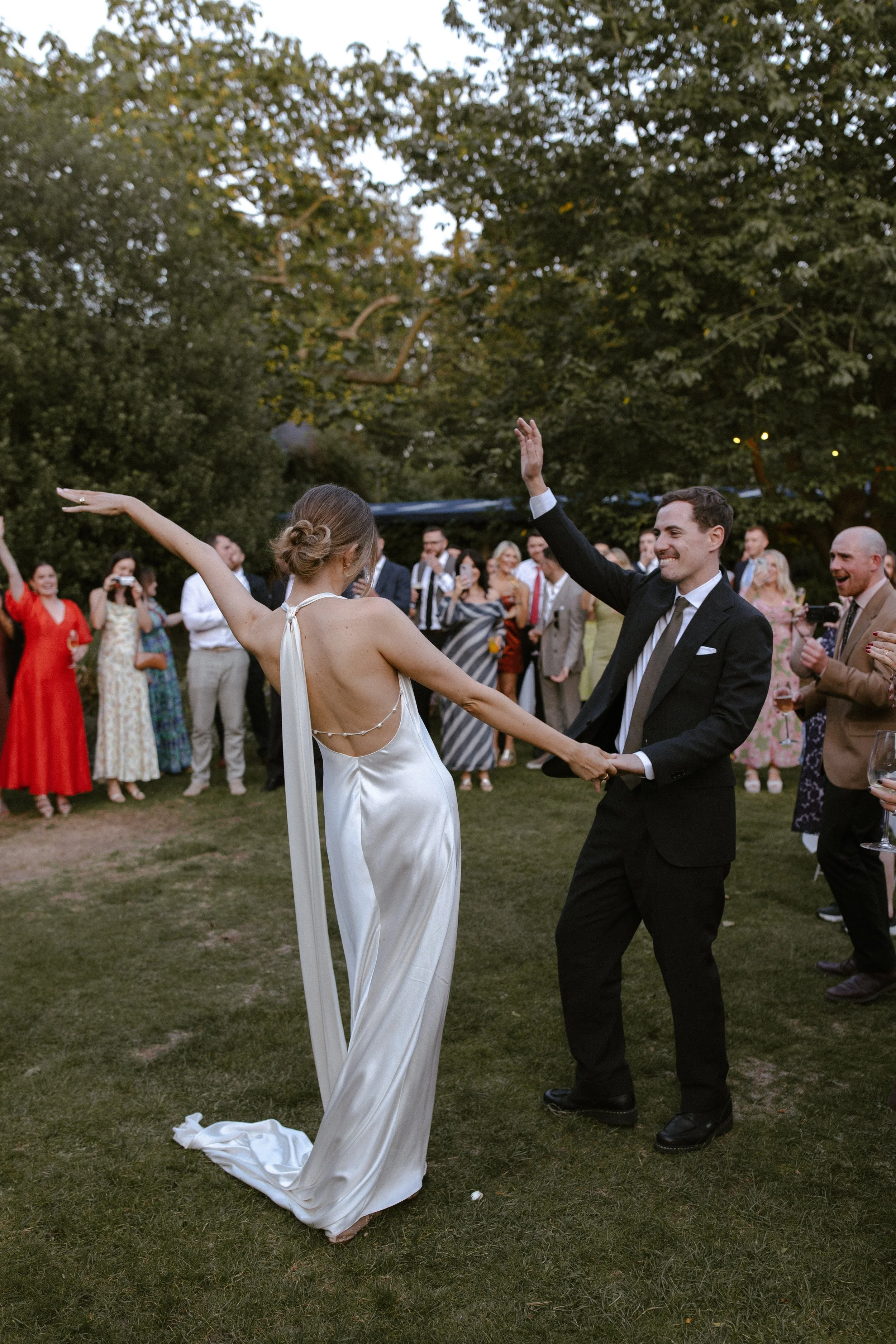 A bride and groom dance together at an outdoor wedding reception, with a crowd of guests in the background.