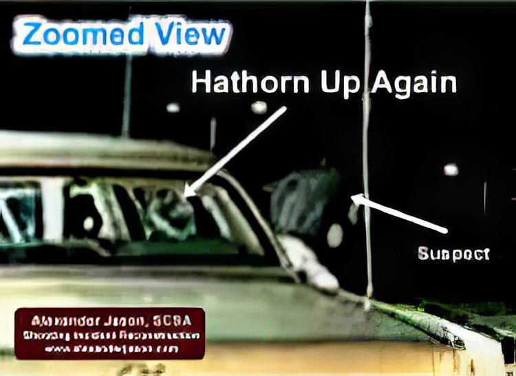 Hawthorn has exited his vehicle and is standing at the open door. Out of view on the left, the suspect points/aims his cell phone.