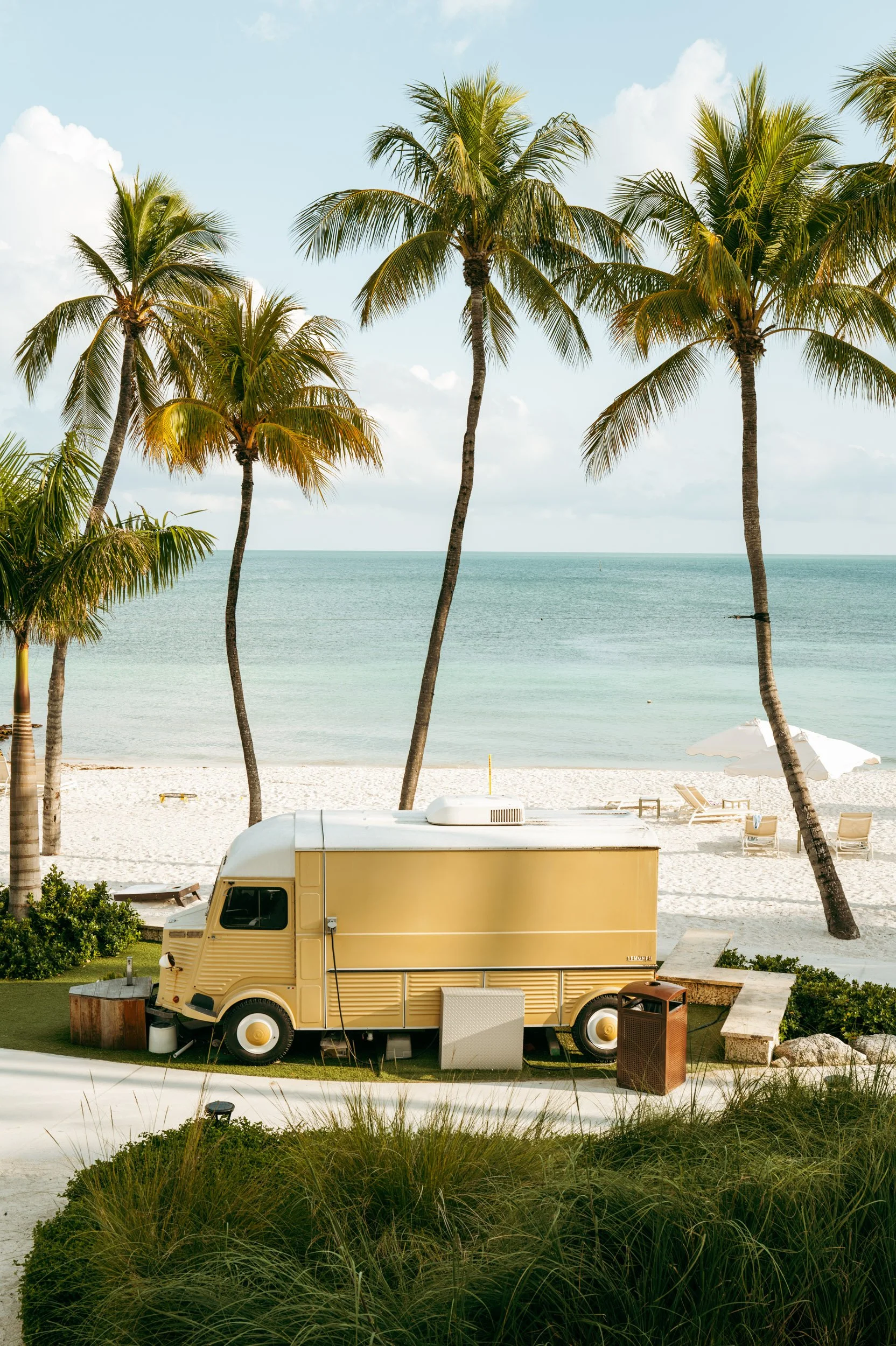 Yellow van parked near palm trees by sandy beach under clear sky in Key West