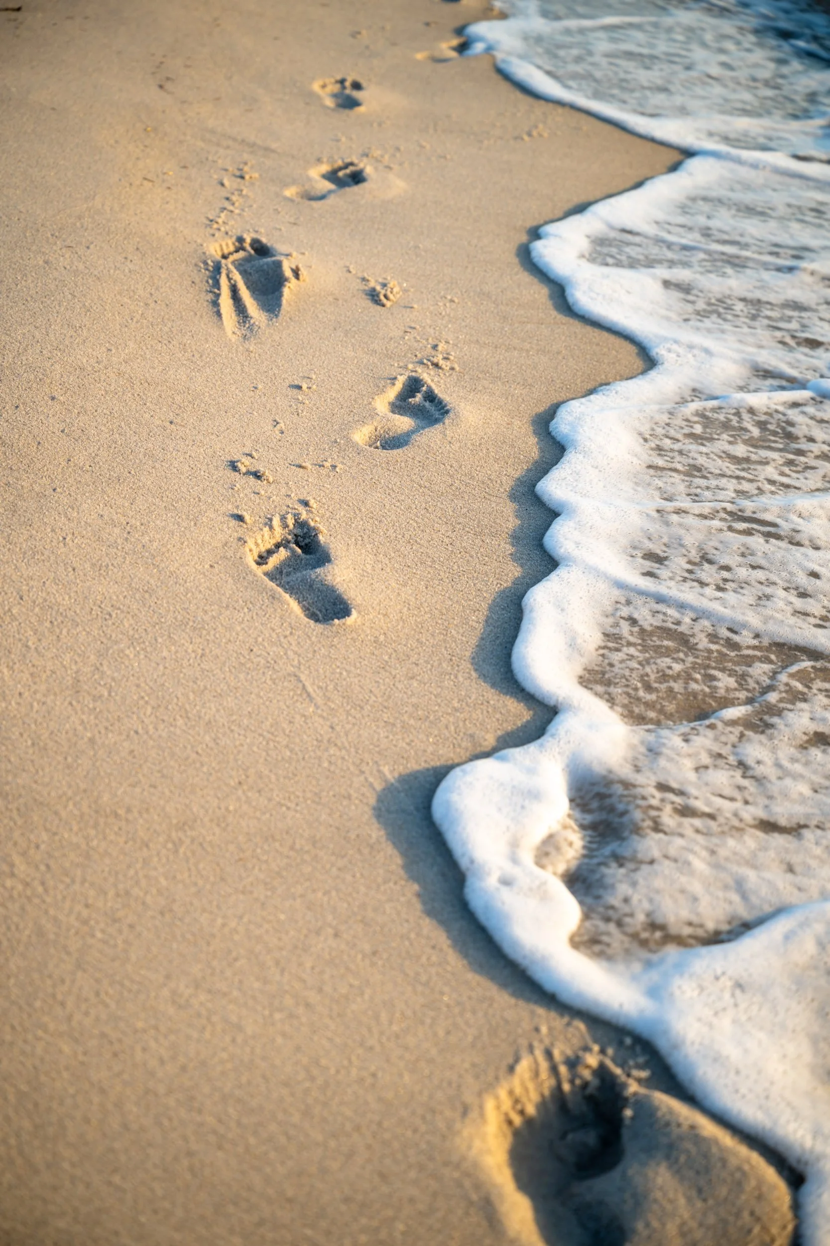 Footprints in soft sand along shoreline with gentle waves and low light in Miami