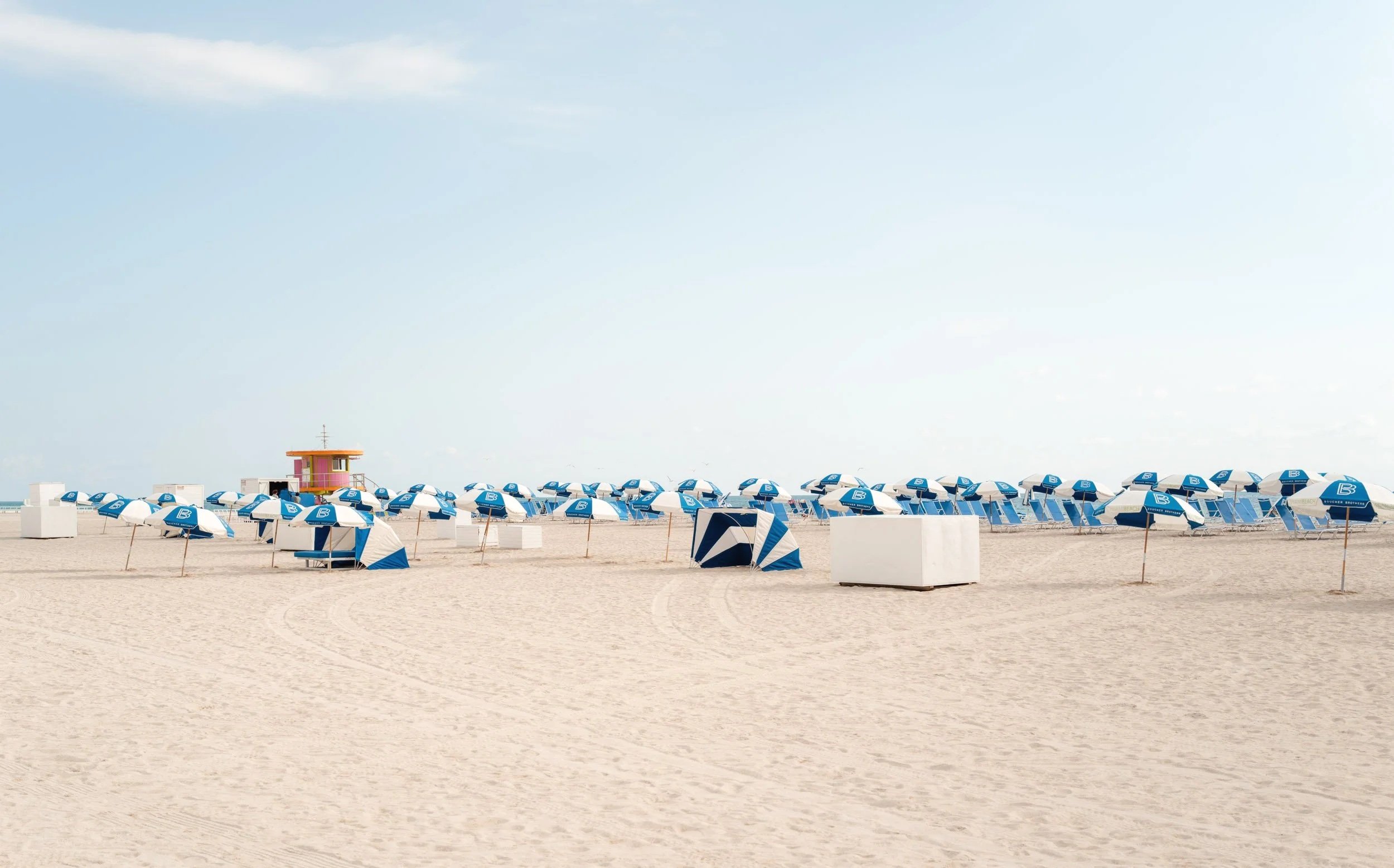 Blue umbrellas and a pink hut on sandy beach with open sea and horizon in Miami