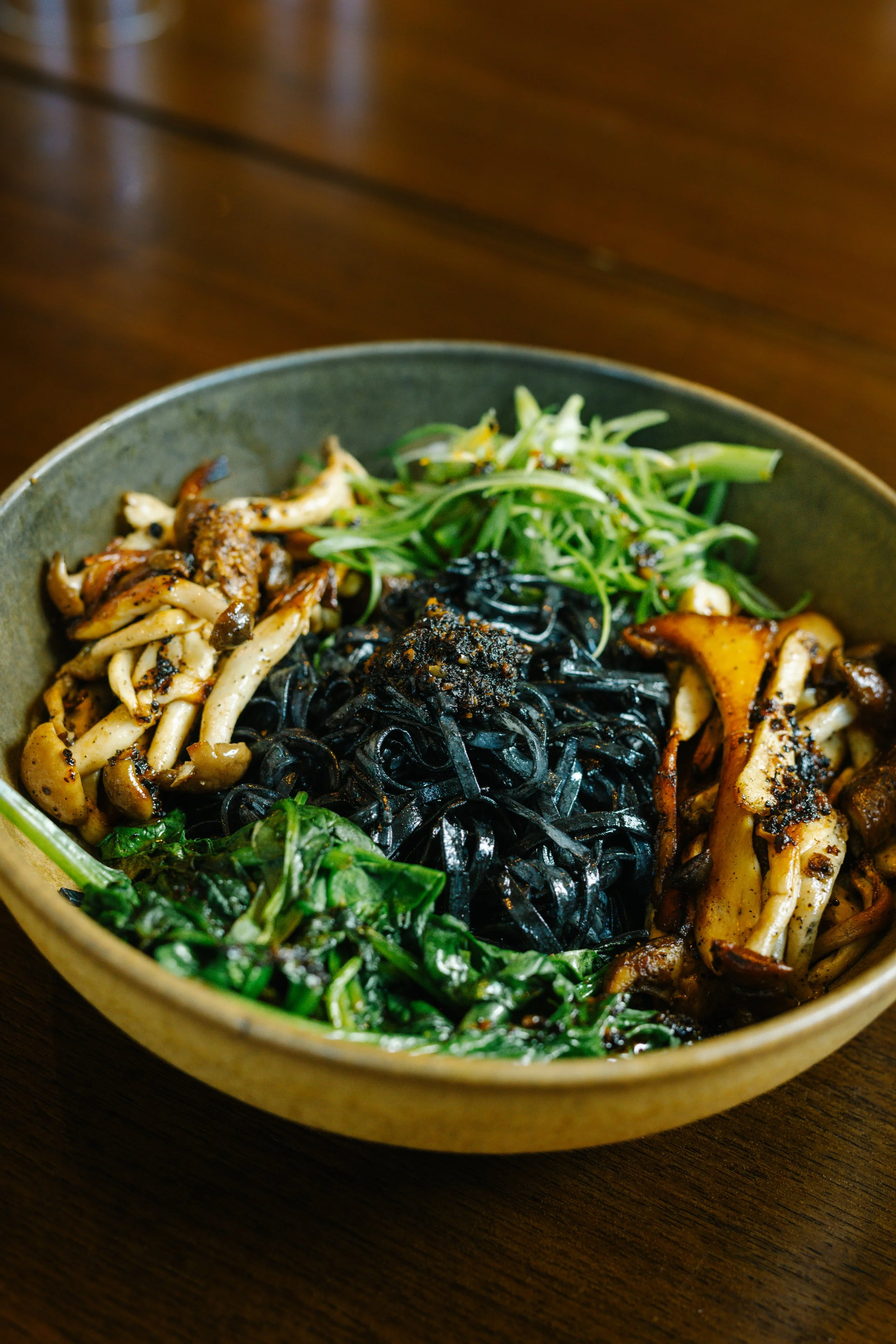 Bowl of mixed Asian noodles with green vegetables and mushrooms.
