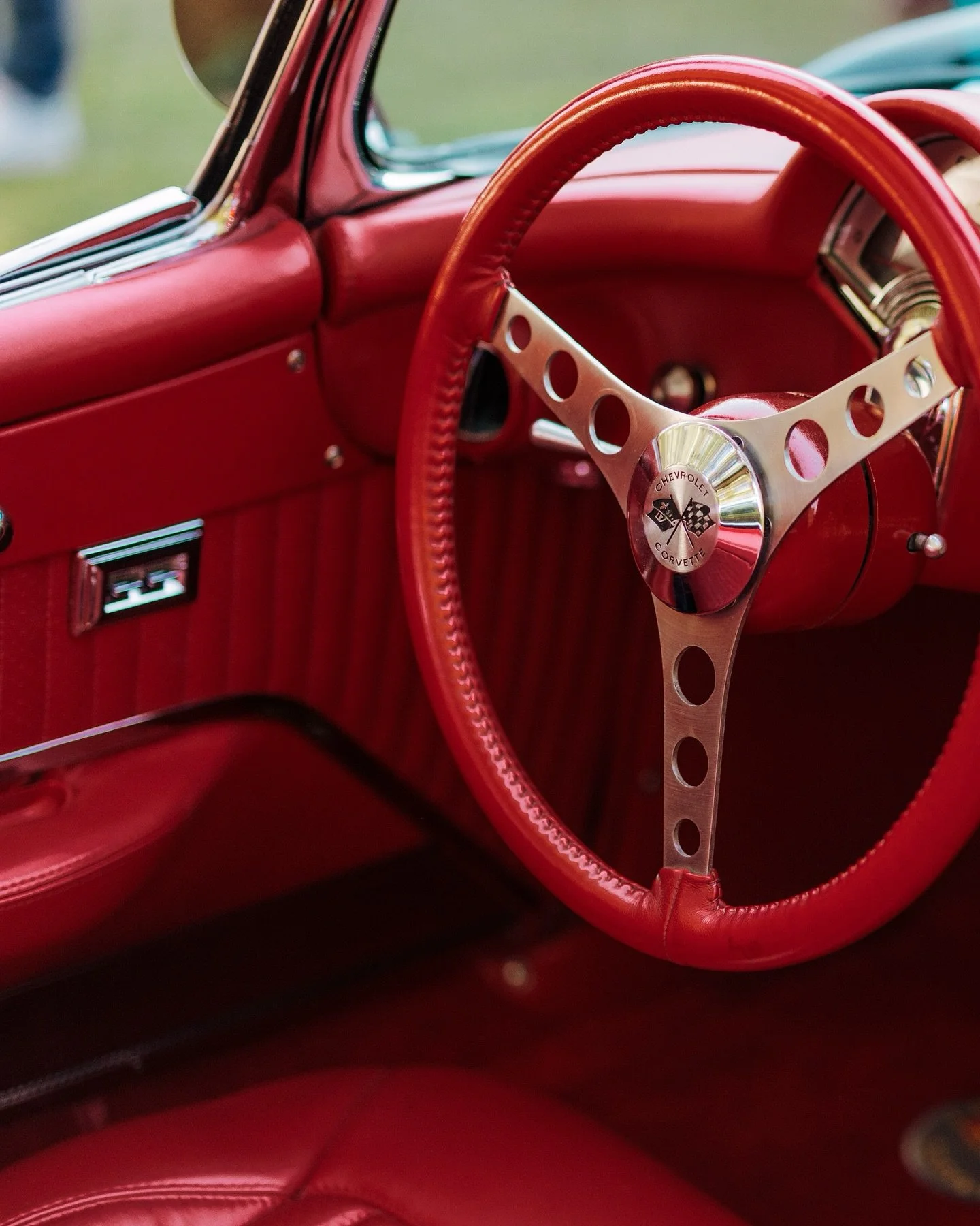 Close-up of a red vintage Chevrolet Corvette interior, showing the steering wheel with Chevrolet and Corvette emblems, and red dashboard and upholstery.