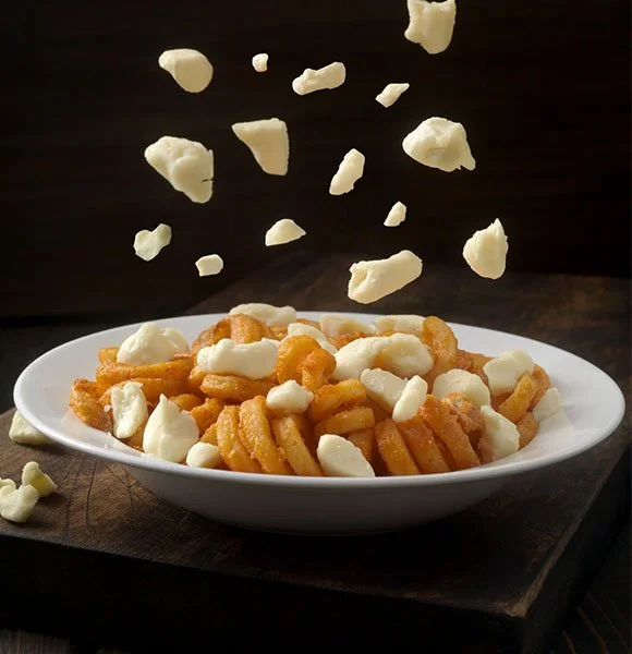 A photo of cheese curds falling onto curly fries to advertise Arby's curly fry poutine.