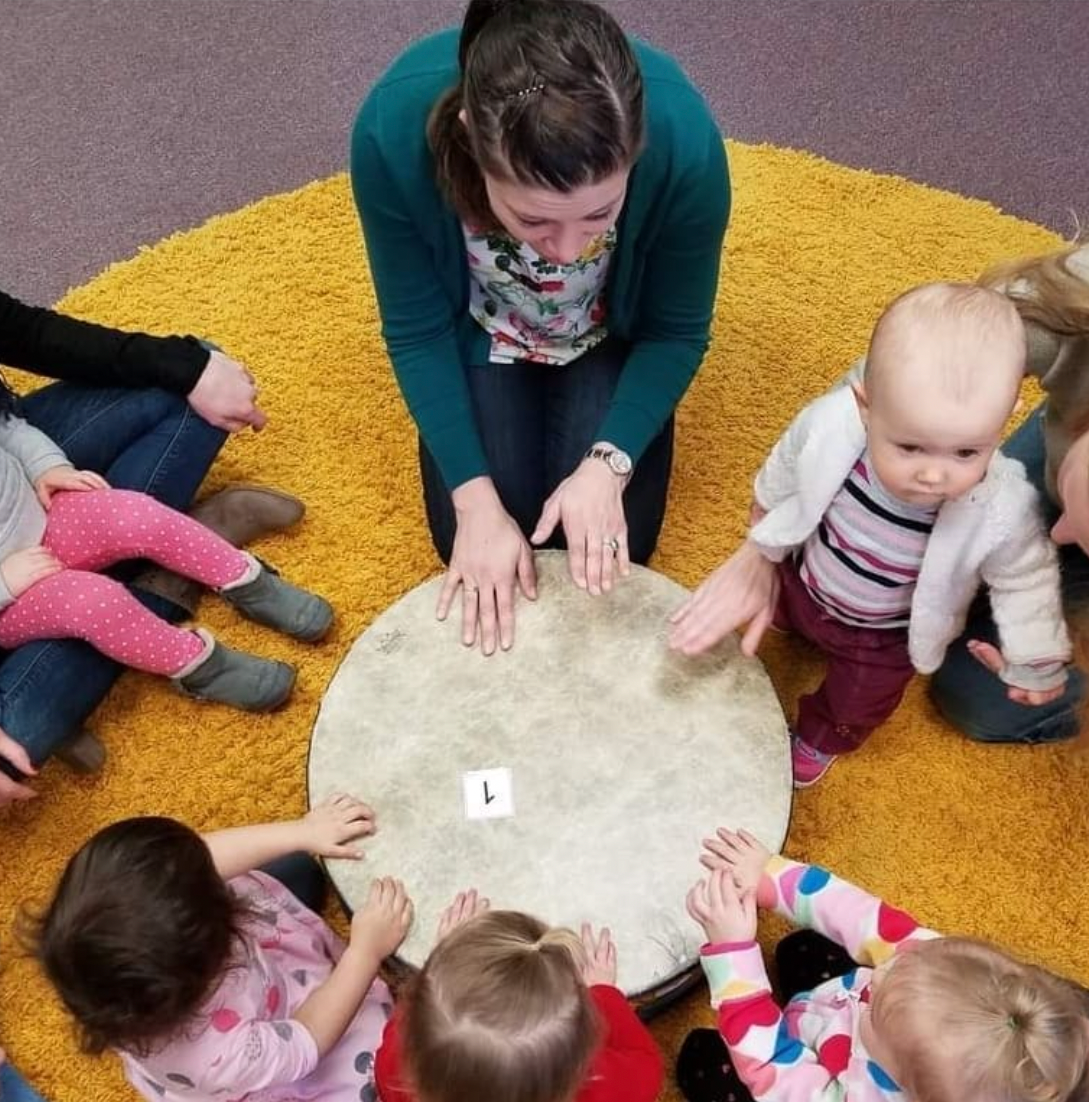 Birds eye view of a music therapist playing a large circular drum with several young children 