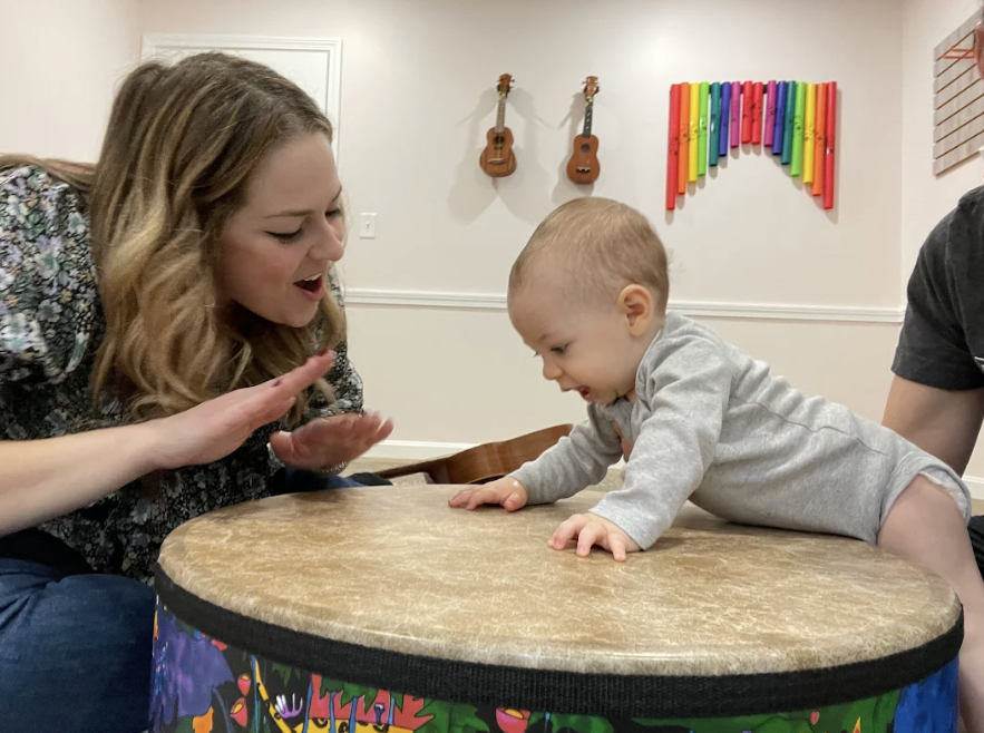 Birds eye view of a music therapist playing a large circular drum with several young children 