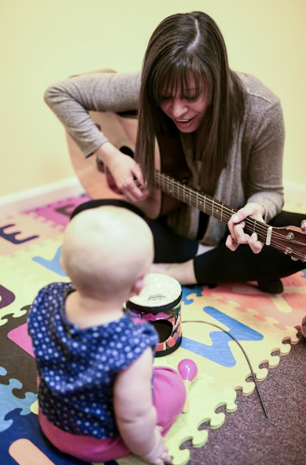 Music therapist playing guitar with an infant during a music therapy session at The Sonatina Center