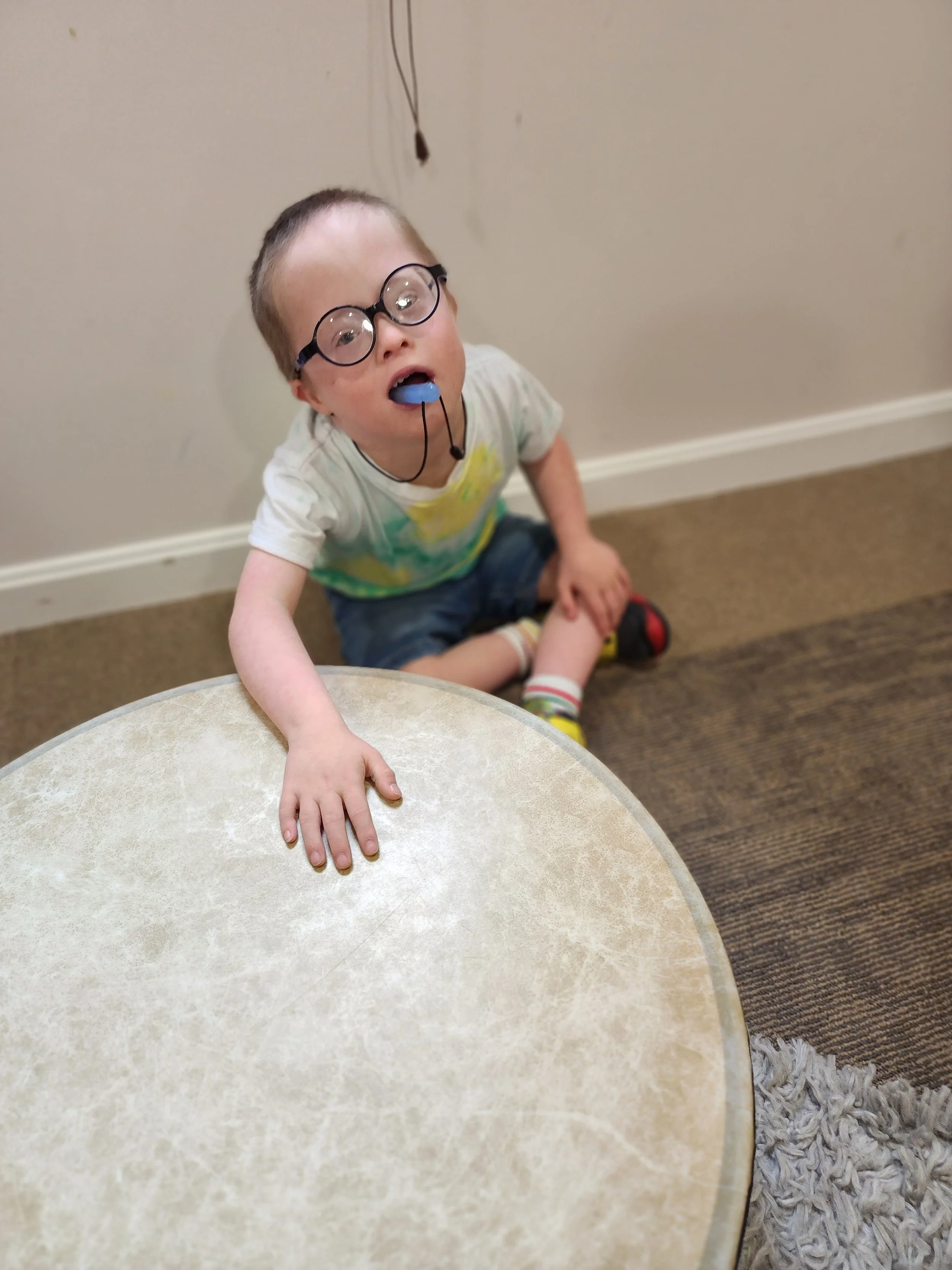 Young child with glasses resting hands on a large drum during music therapy at The Sonatina Center