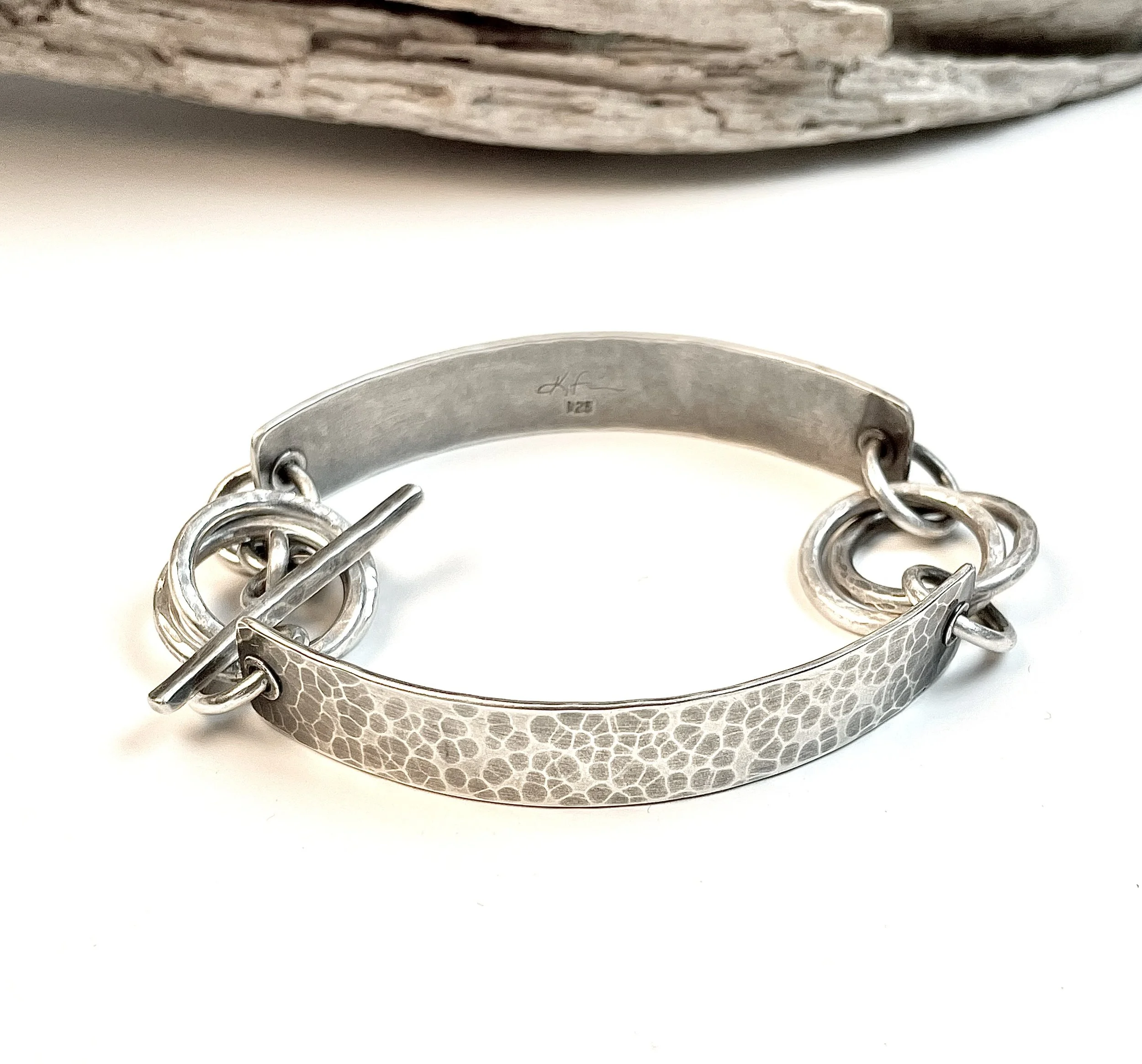Hand-textured sterling silver is connected to interlocking rings and finished with a hand crafted toggle. Oxidized to highlight texture. 
Gorgeous on its own or layered with other bracelets.