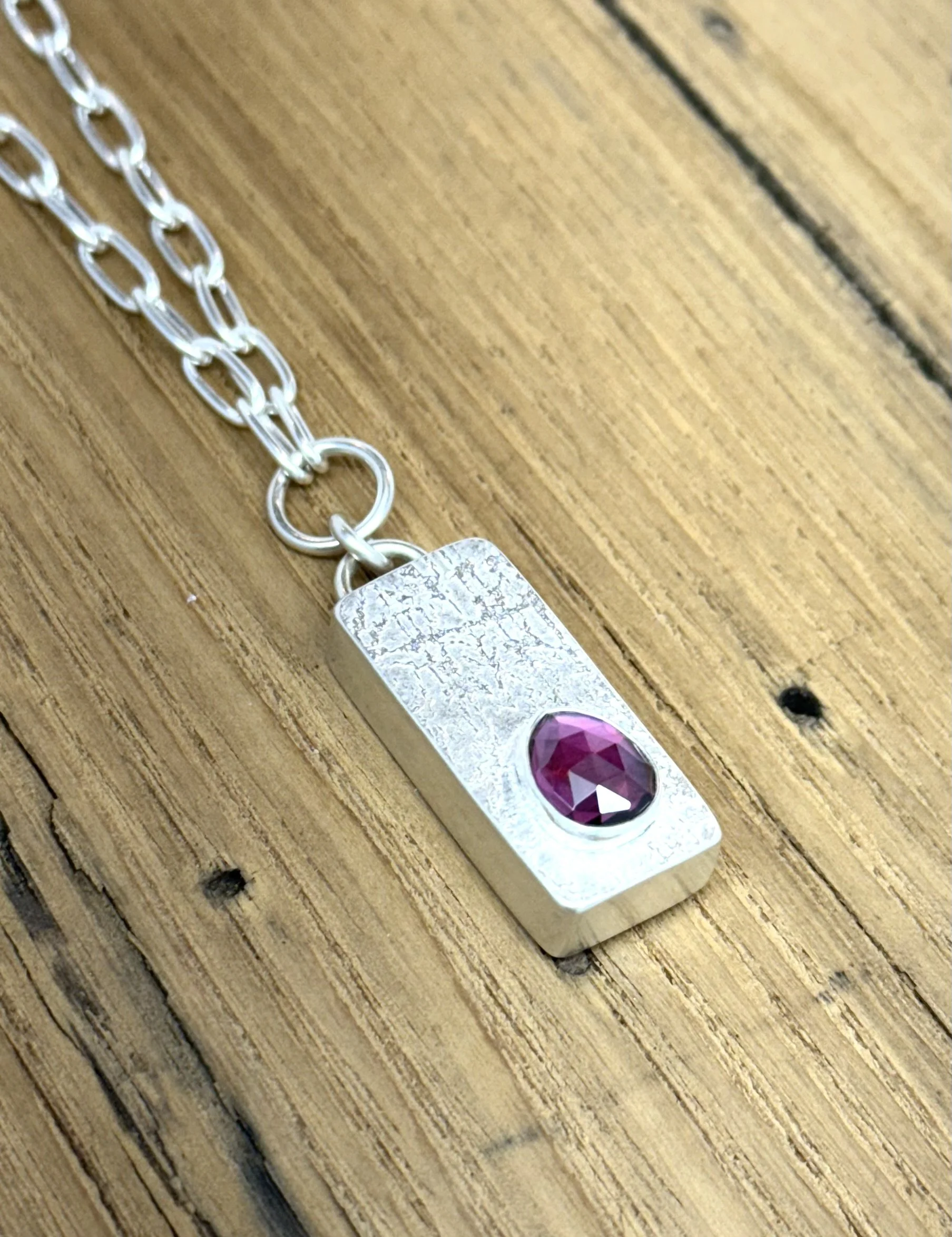 Close-up of handcrafted Keystone Pendant in sterling silver, showcasing a faceted oval blue sapphire set in textured silver. Artisan gemstone necklace by KFinn Designs.