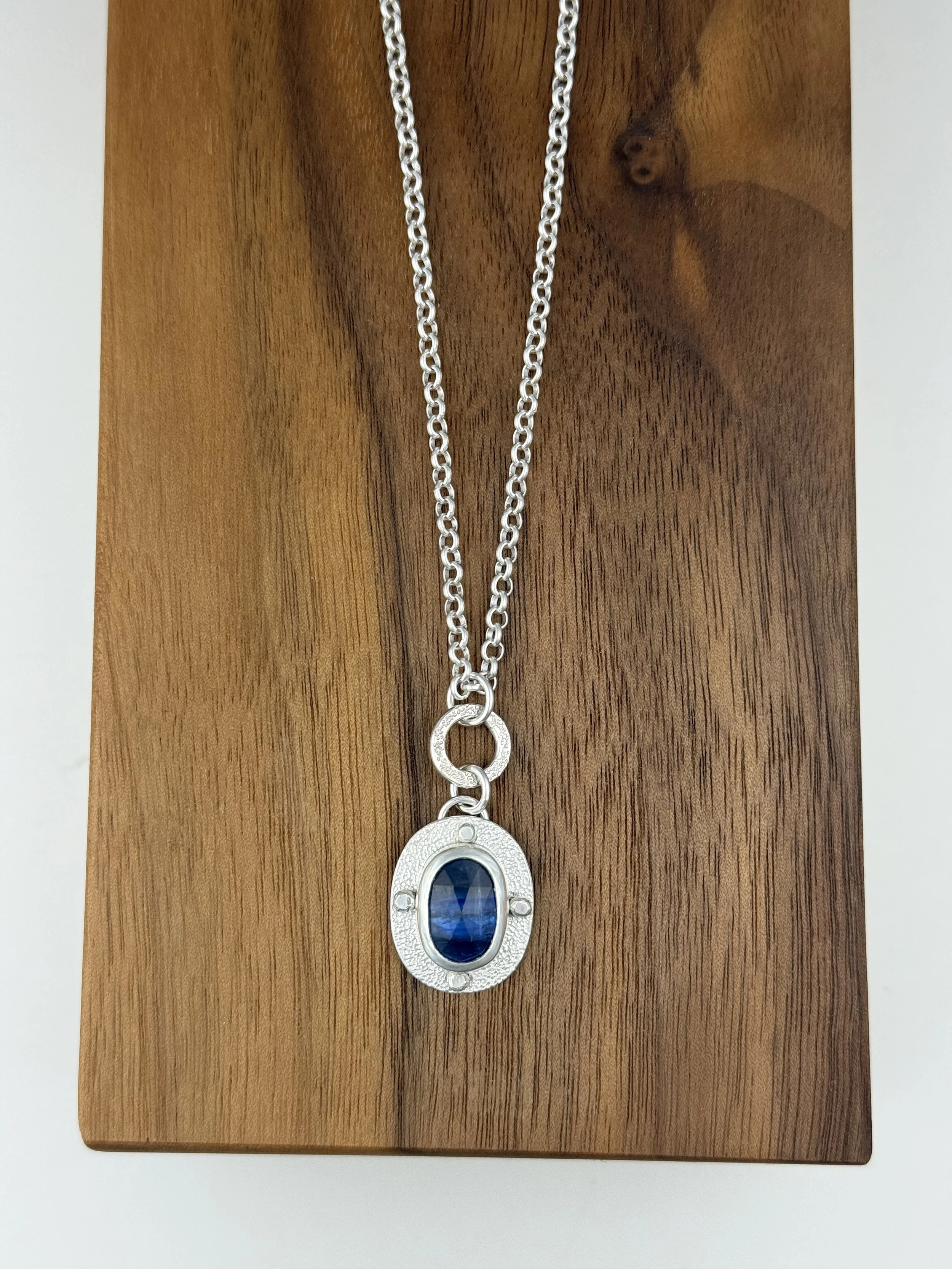 Modern Relic oval kyanite pendant lying flat on wood.jpg