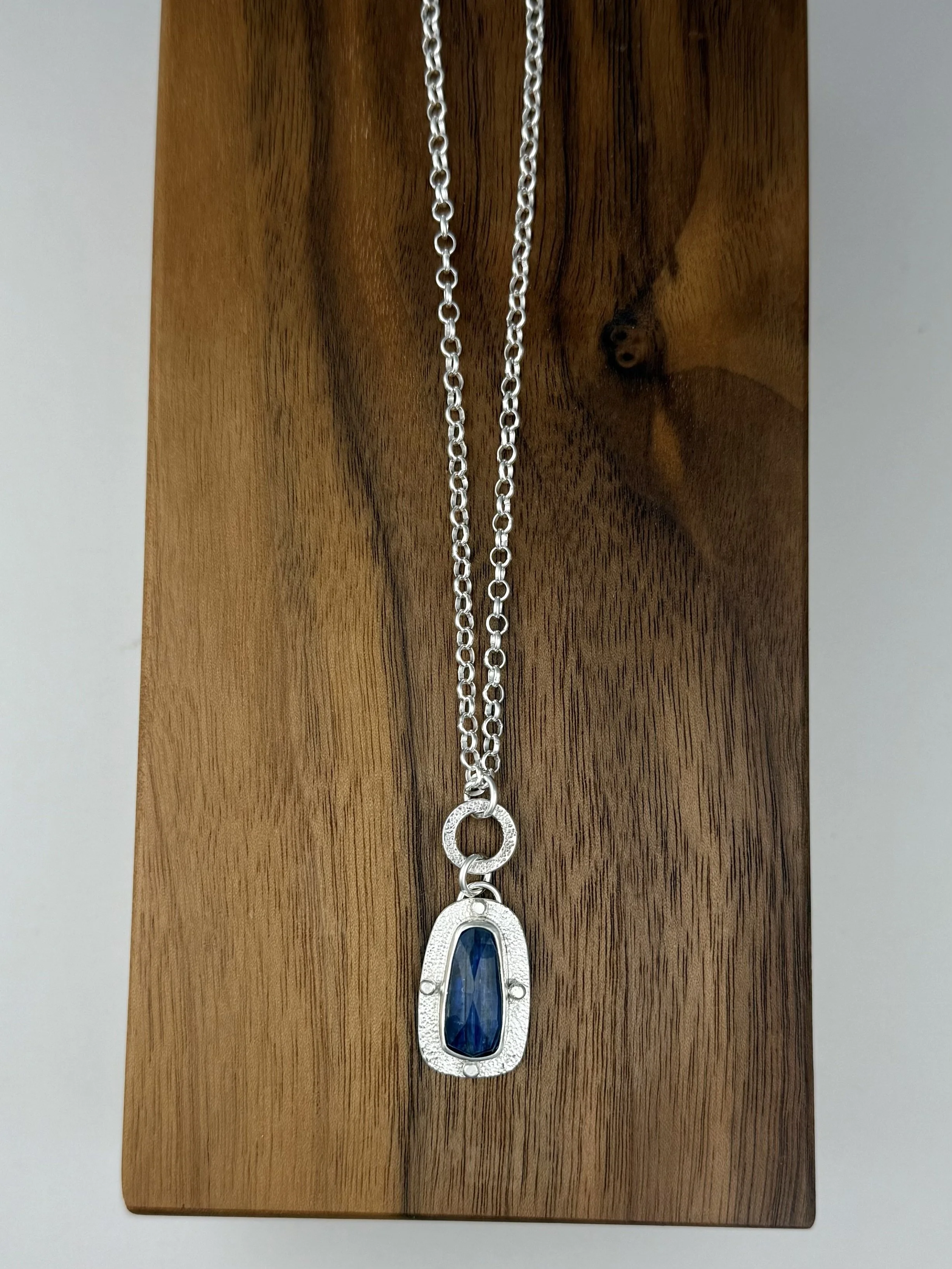 Modern Relic long kyanite pendant lying flat on wood.jpg