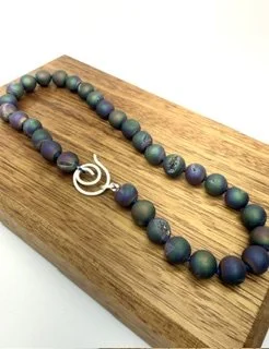Northern Lights Necklace displayed on wood, highlighting the iridescent druzy quartz beads and hand-forged sterling siler spiral clasp.