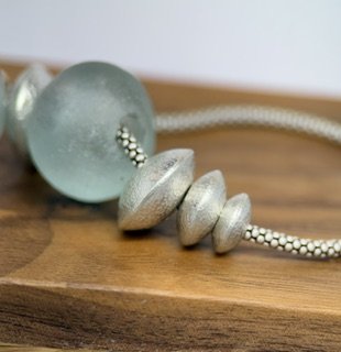 Close-up of handcrafted textured sterling silver beads and vintage blue-green glass in the Stillwater Necklace