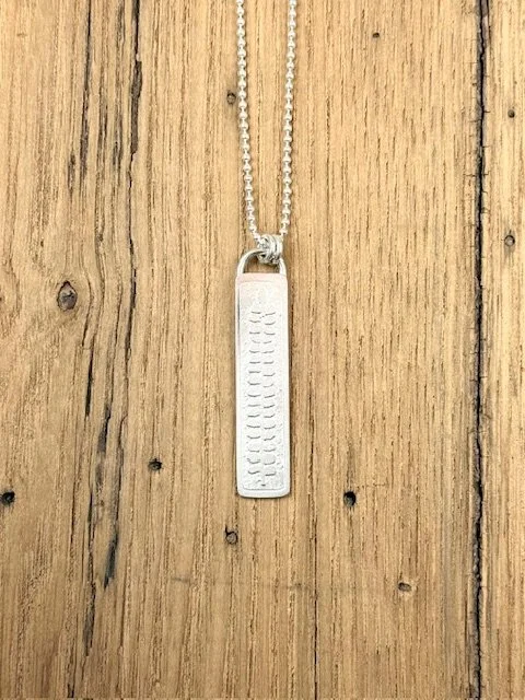 Close-up of KFinn Designs Botanica Collection long pendant necklace, artisan silver pendant with nature-inspired etched details.