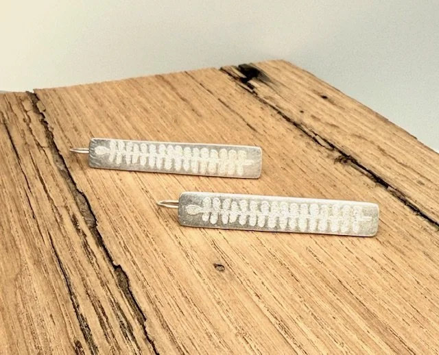 Pair of silver rectangular earrings with etched botanical patterns, displayed flat on a wooden surface