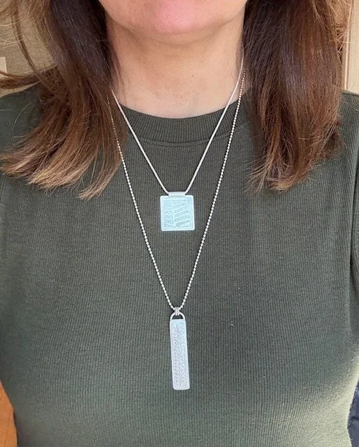Layered Botanica Collection necklaces in sterling silver, square etched pendant and long pendant worn together, artisan design by KFinn Designs.
