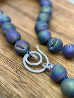 Detail view of rainbow druzy quartz beads with sparkling crystal pockets, blue silk knots, and a hand-forged sterling silver clasp.