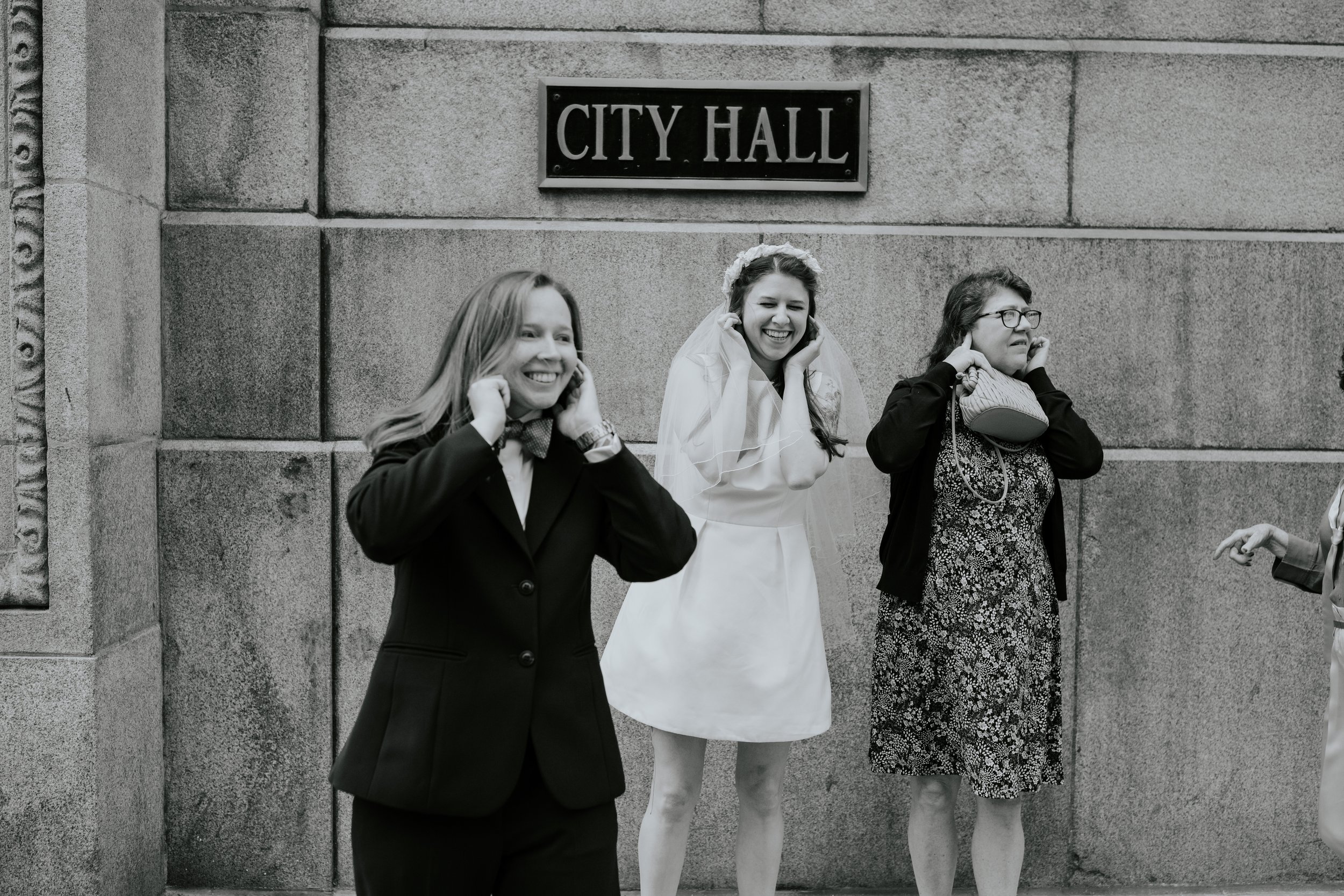 The wedding couple stand with one of their mothers in front of City Hall as a firetruck passes.