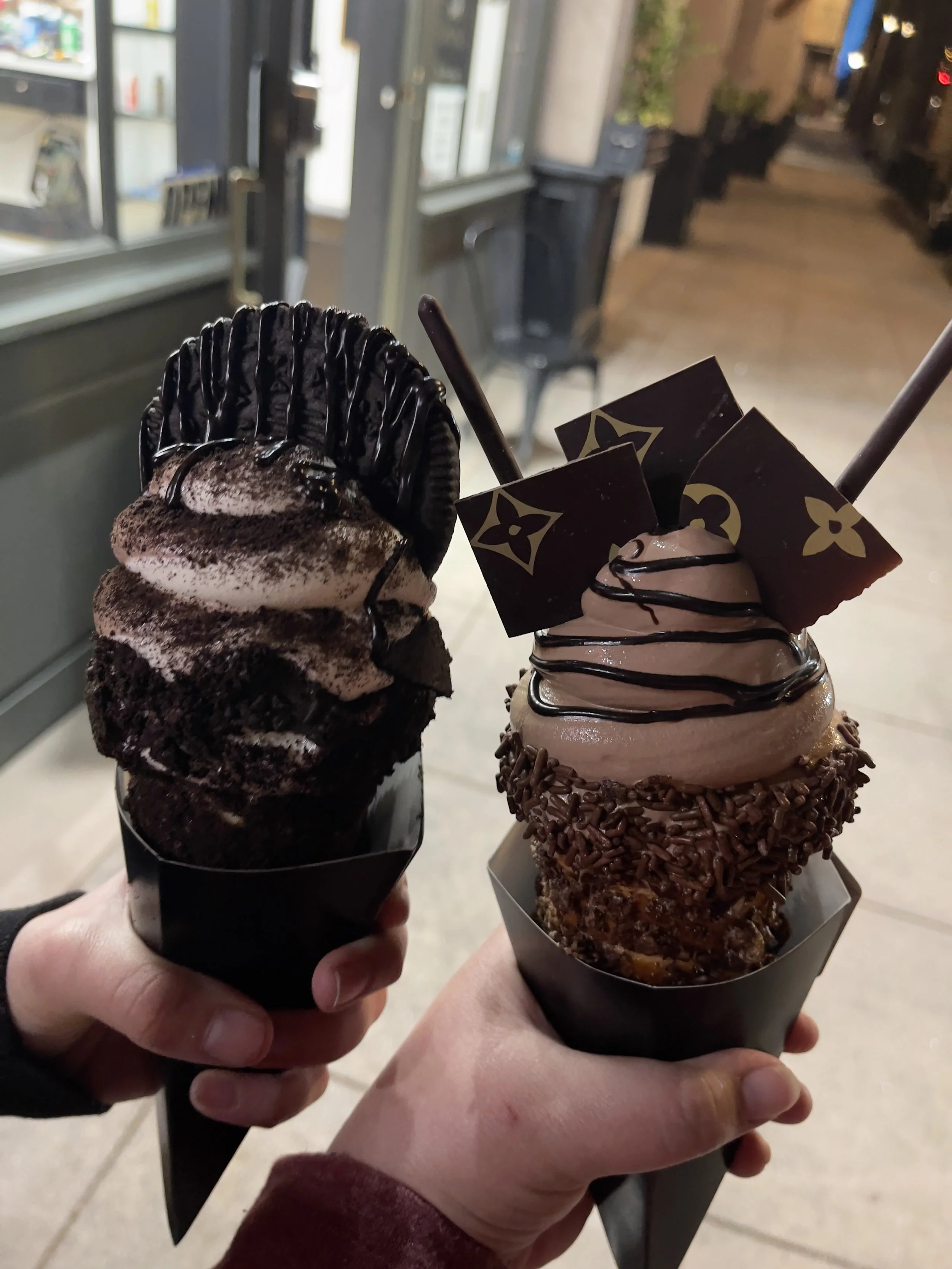 Two hands hold two decadent ice cream cones.