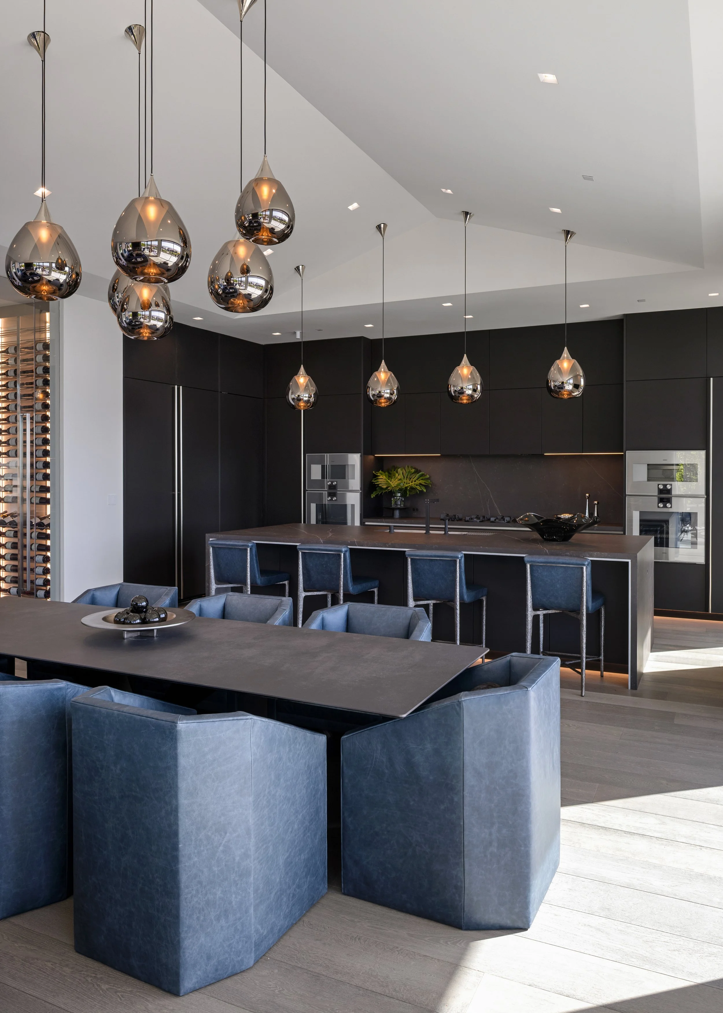 Modern kitchen with black cabinetry, a large island with bar stools, and pendant lights hanging from the ceiling.