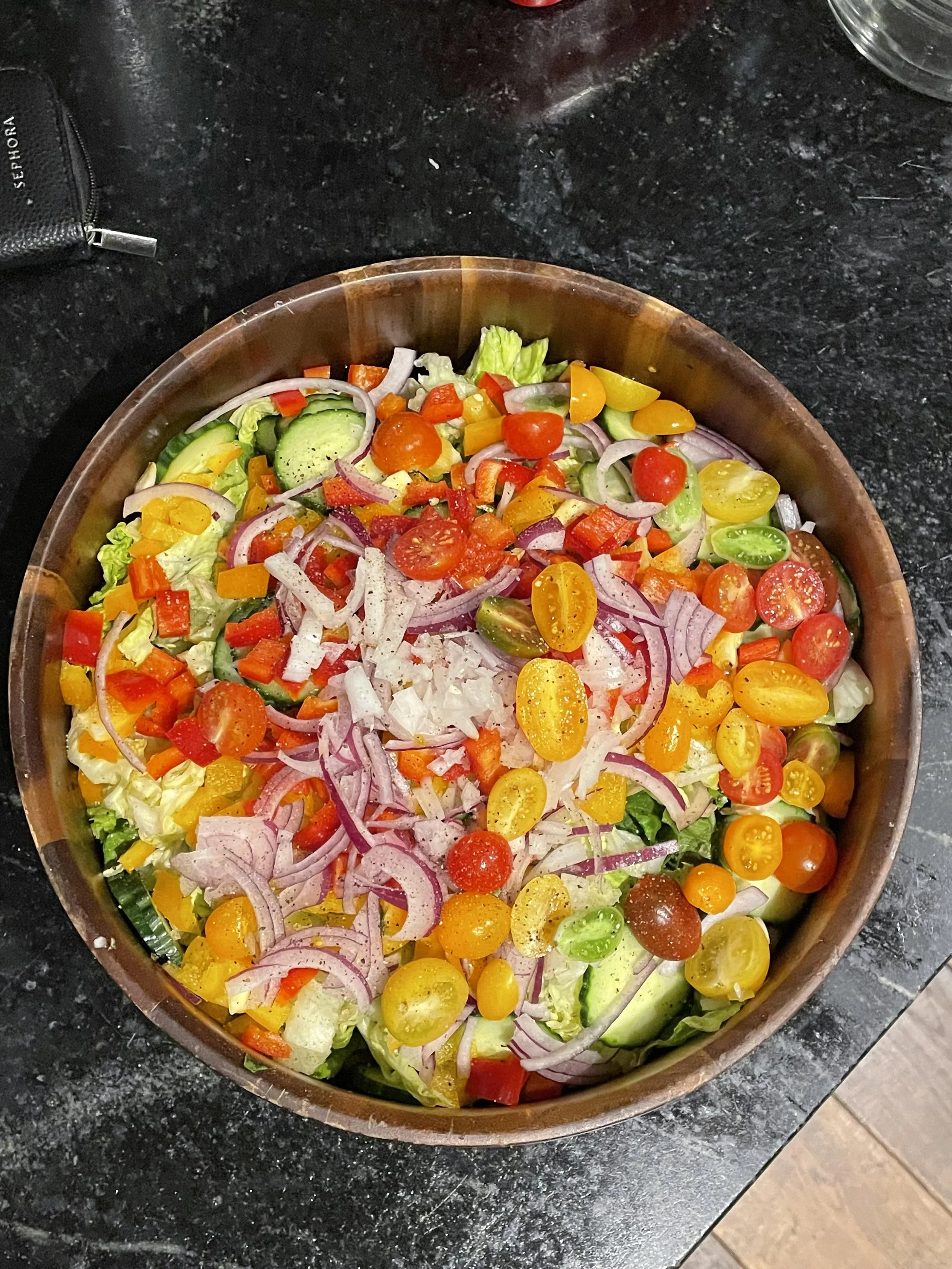 A large bowl filled with a colorful salad containing lettuce, cherry tomatoes, sliced cucumbers, red onions, and chopped bell peppers in red, yellow, and green.