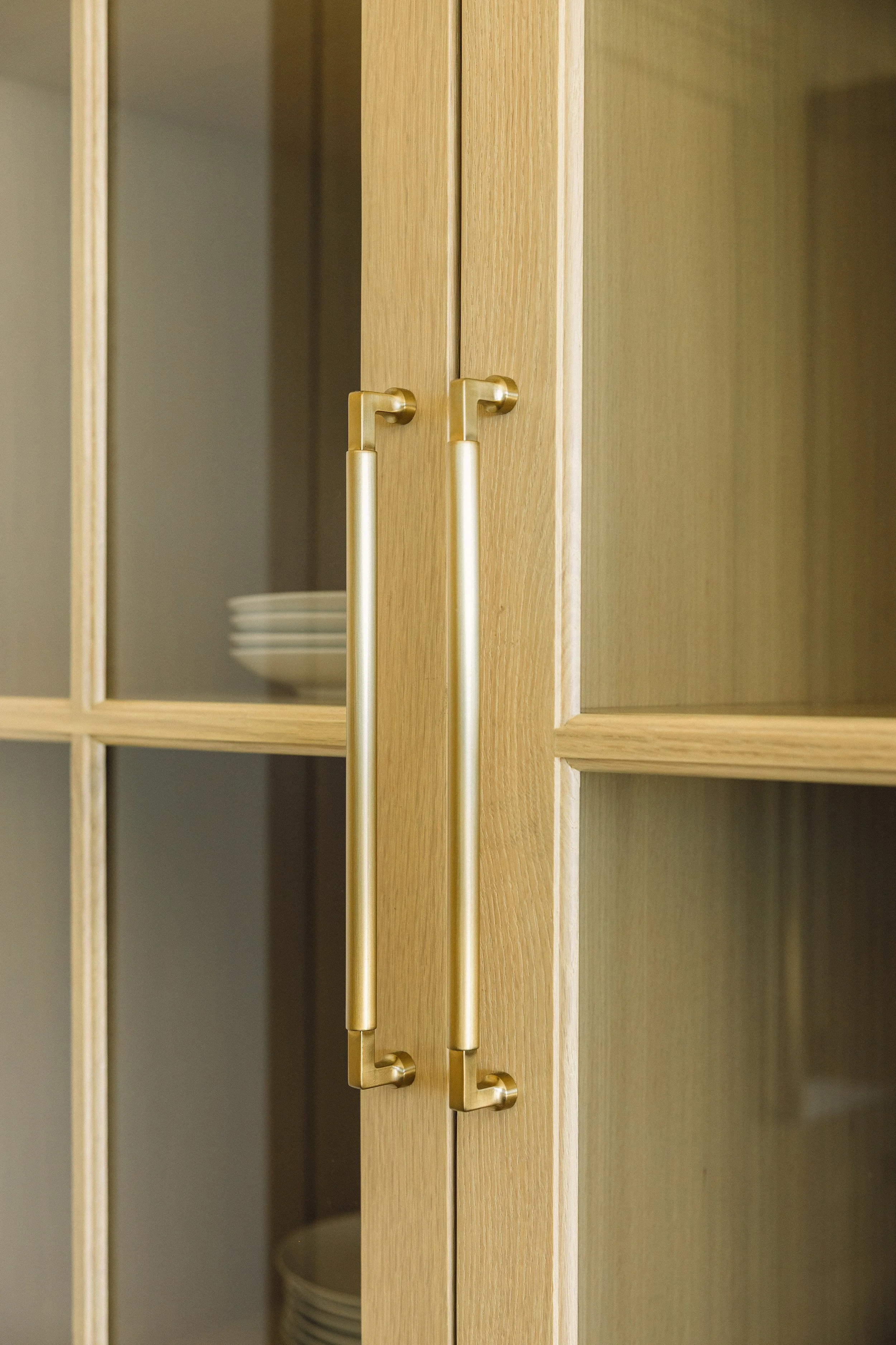 Close-up of wooden cabinet doors with gold handles, slightly open to reveal dishes inside.