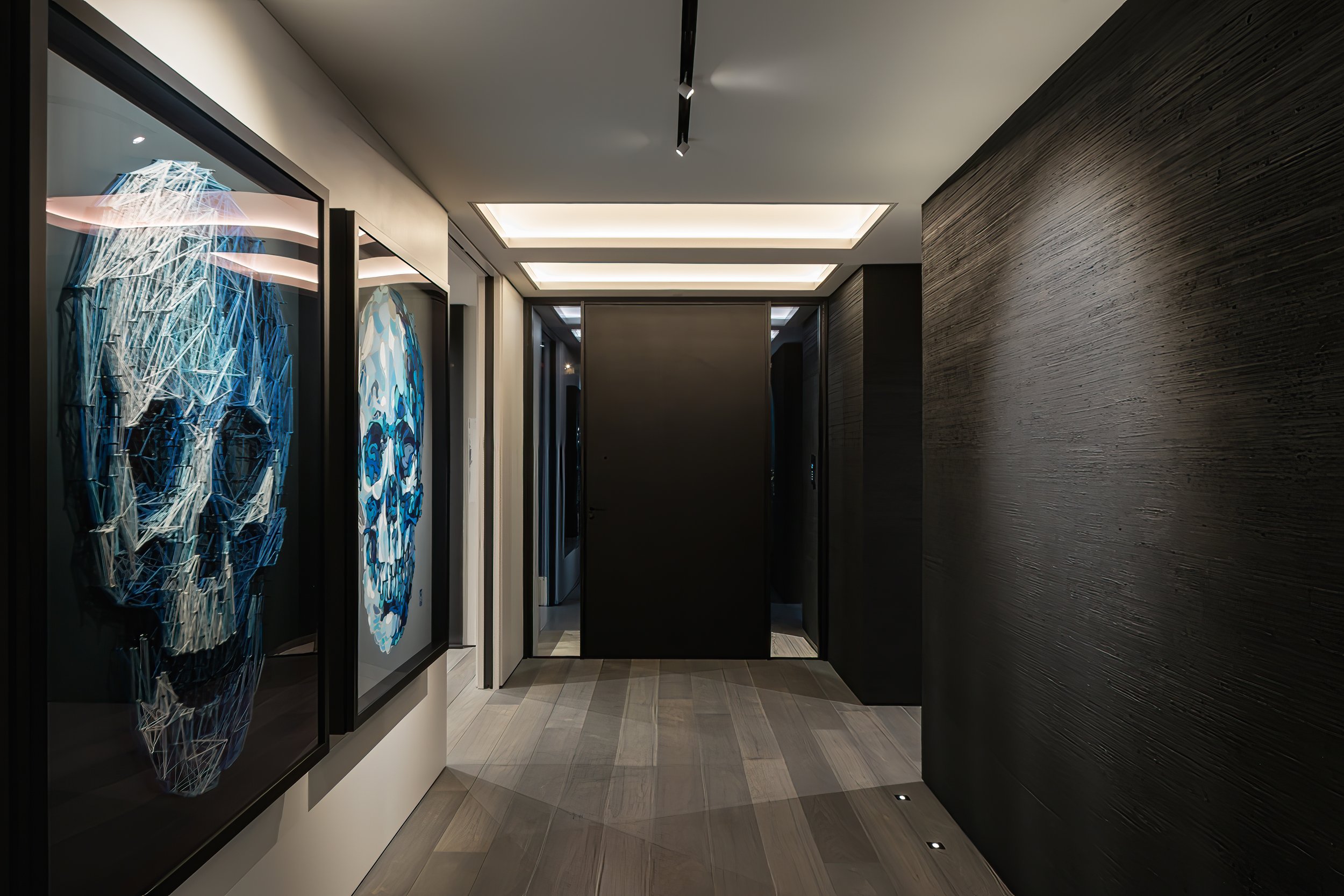 Hallway with modern artwork of a skull and a face in geometric style, illuminated ceiling lights, dark textured wall, and tiled floor.