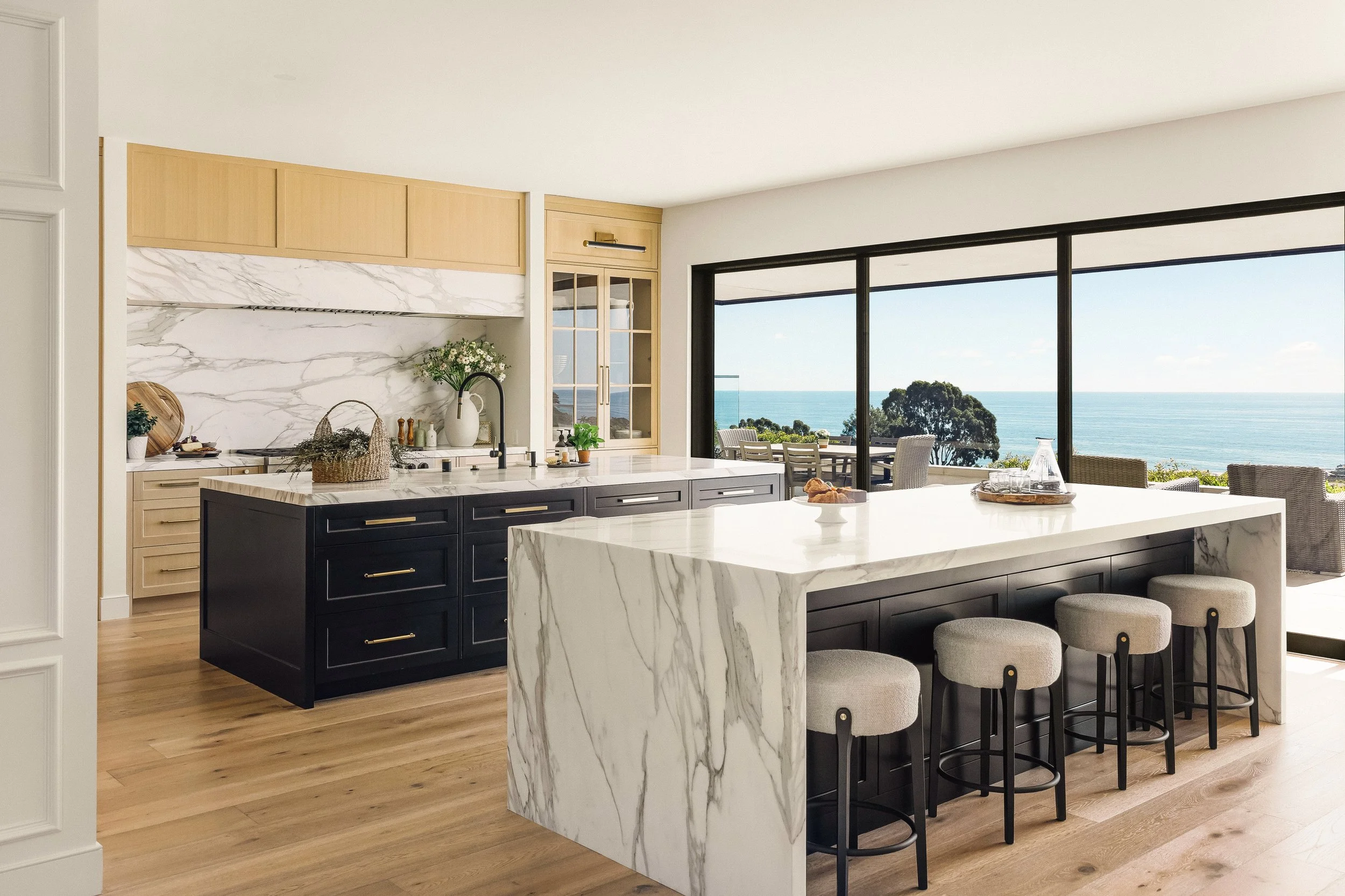 Modern kitchen with black and white marble countertops, a large marble island with stools, and a view of the ocean through large glass sliding doors.