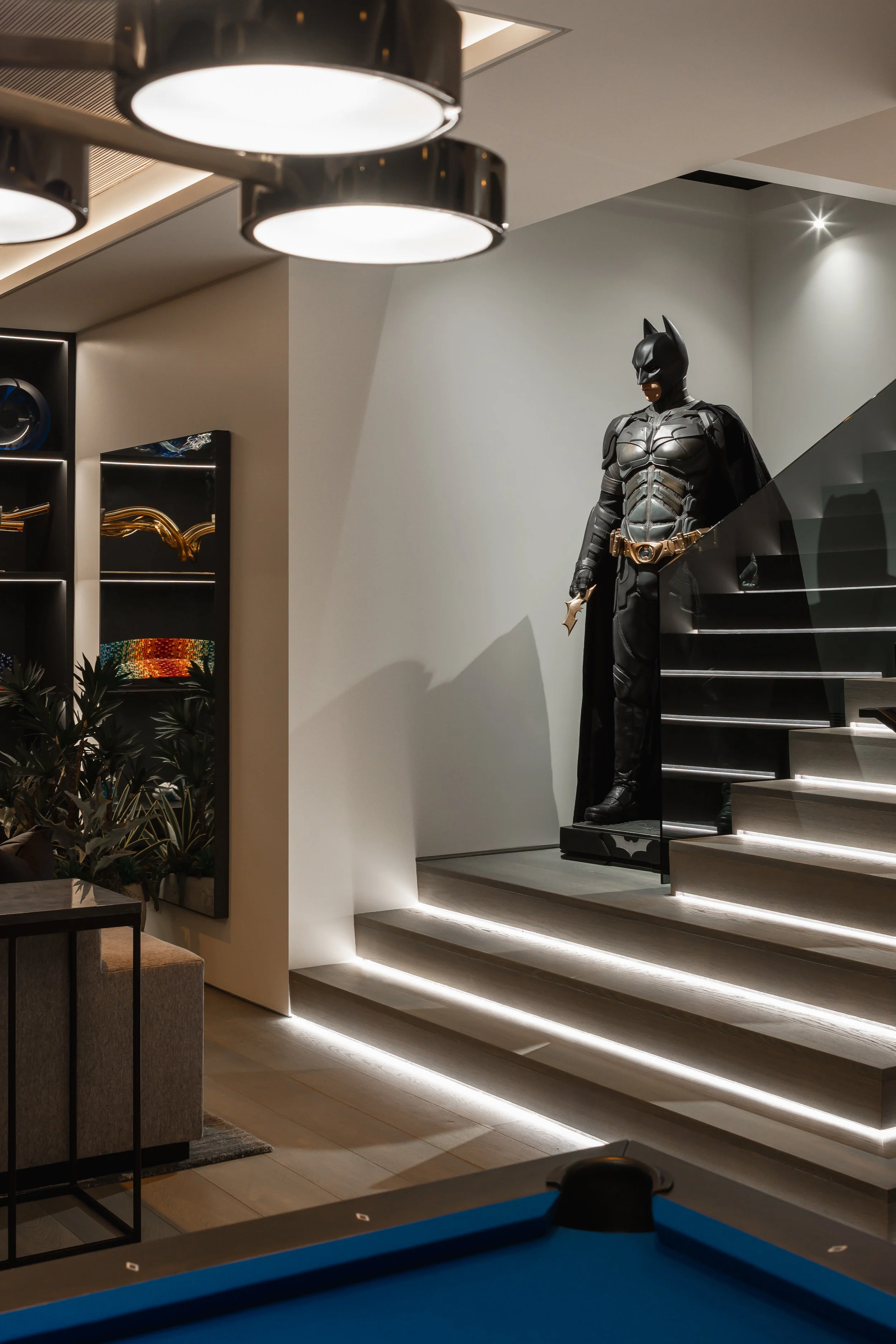 A life-sized Batman statue on a staircase landing in a modern, well-lit interior space.
