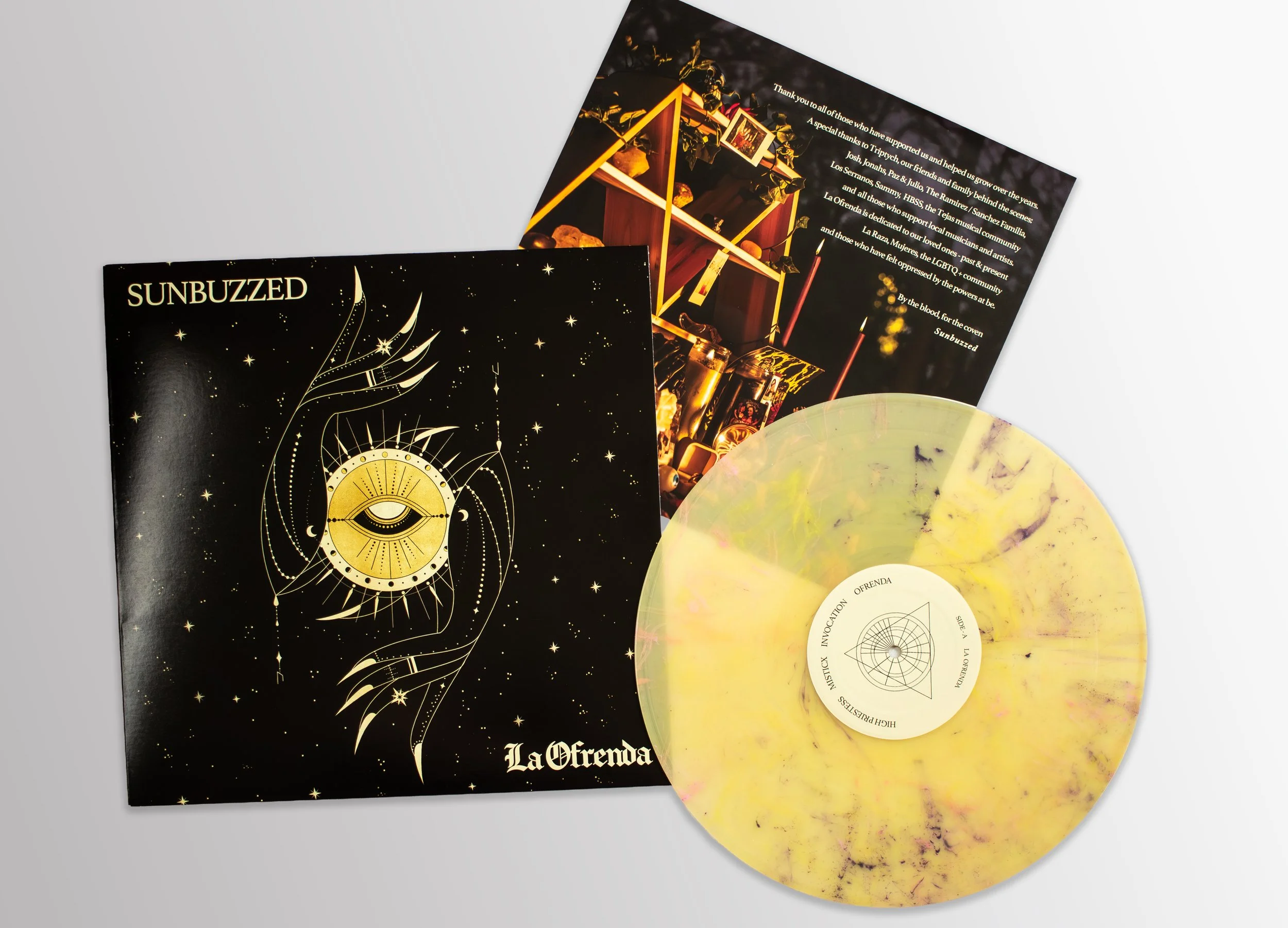 A vinyl record titled 'La Ofrena' with its cover art featuring a golden eye within a circular design, surrounded by a starry night sky. There is also an informational pamphlet with a photograph of sacred objects, including candles and religious artif