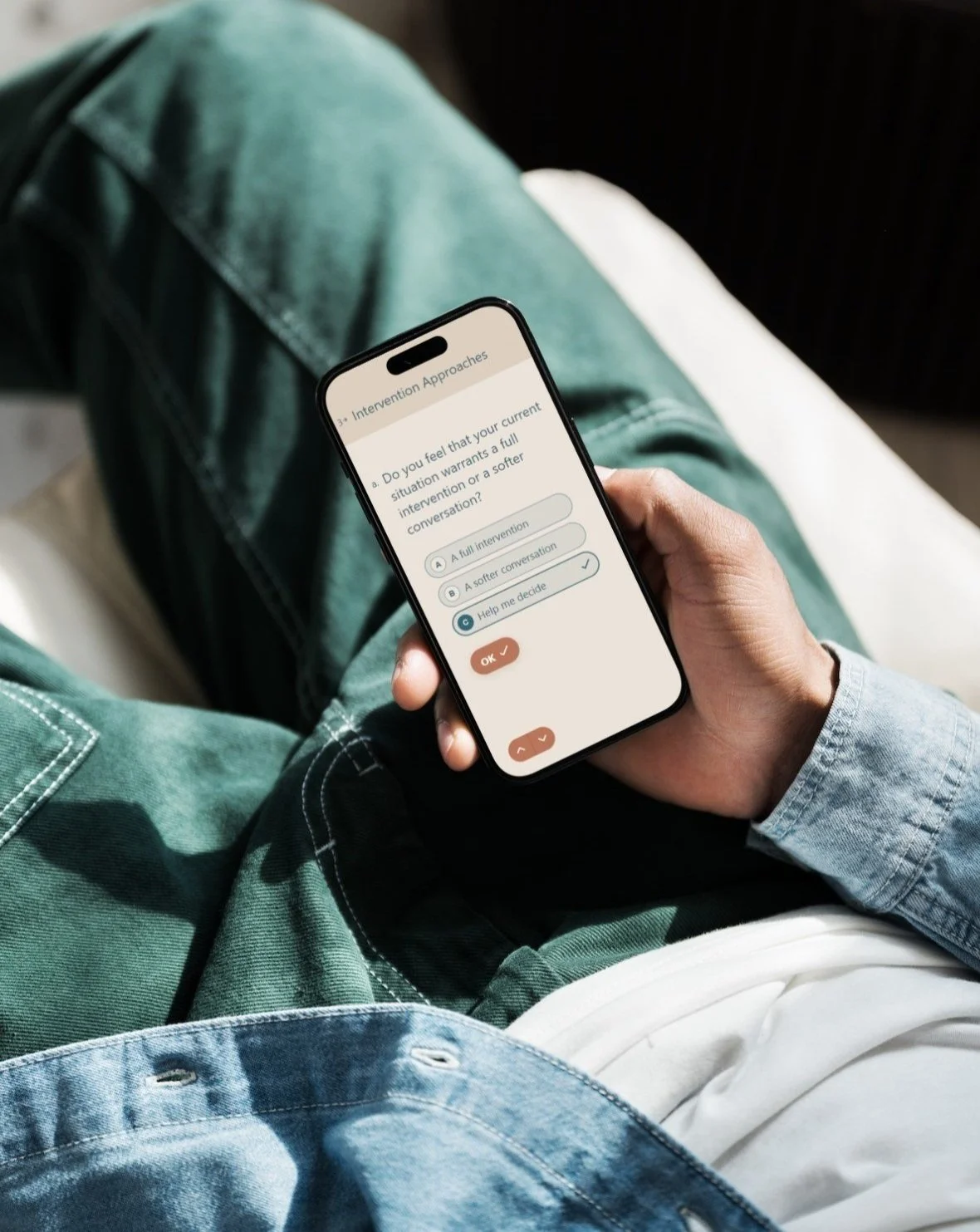 Person sitting on a bed holding a smartphone and using a mental health app to answer questions about intervention approaches.