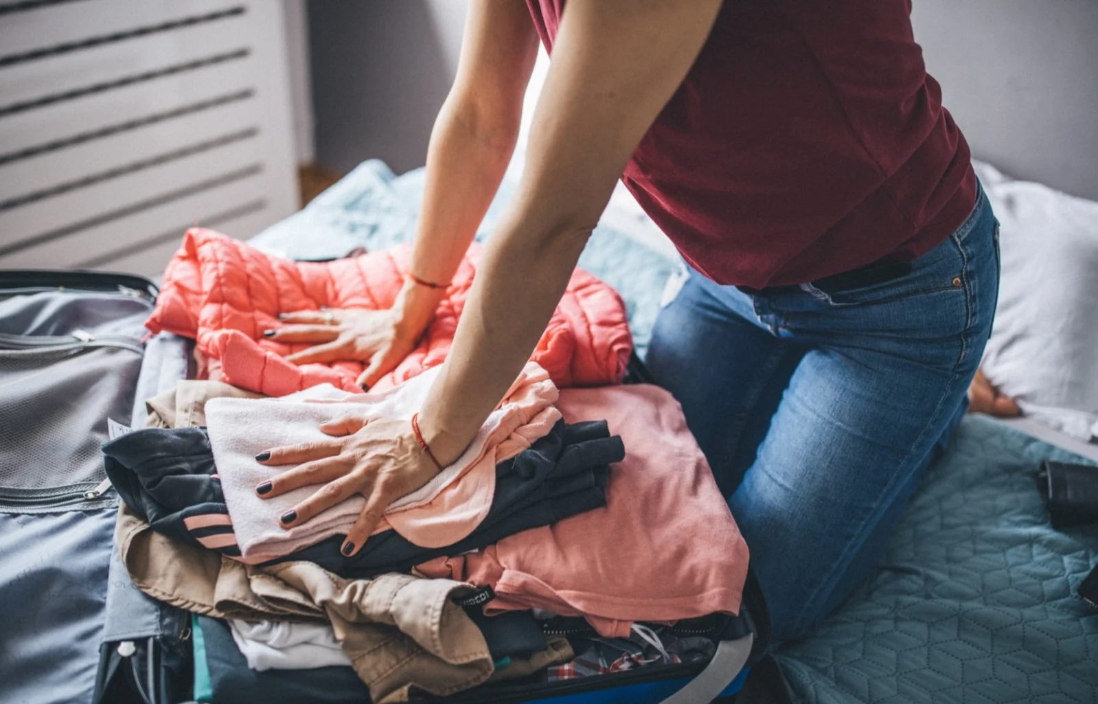 Person packing clothes into an open suitcase on a bed.