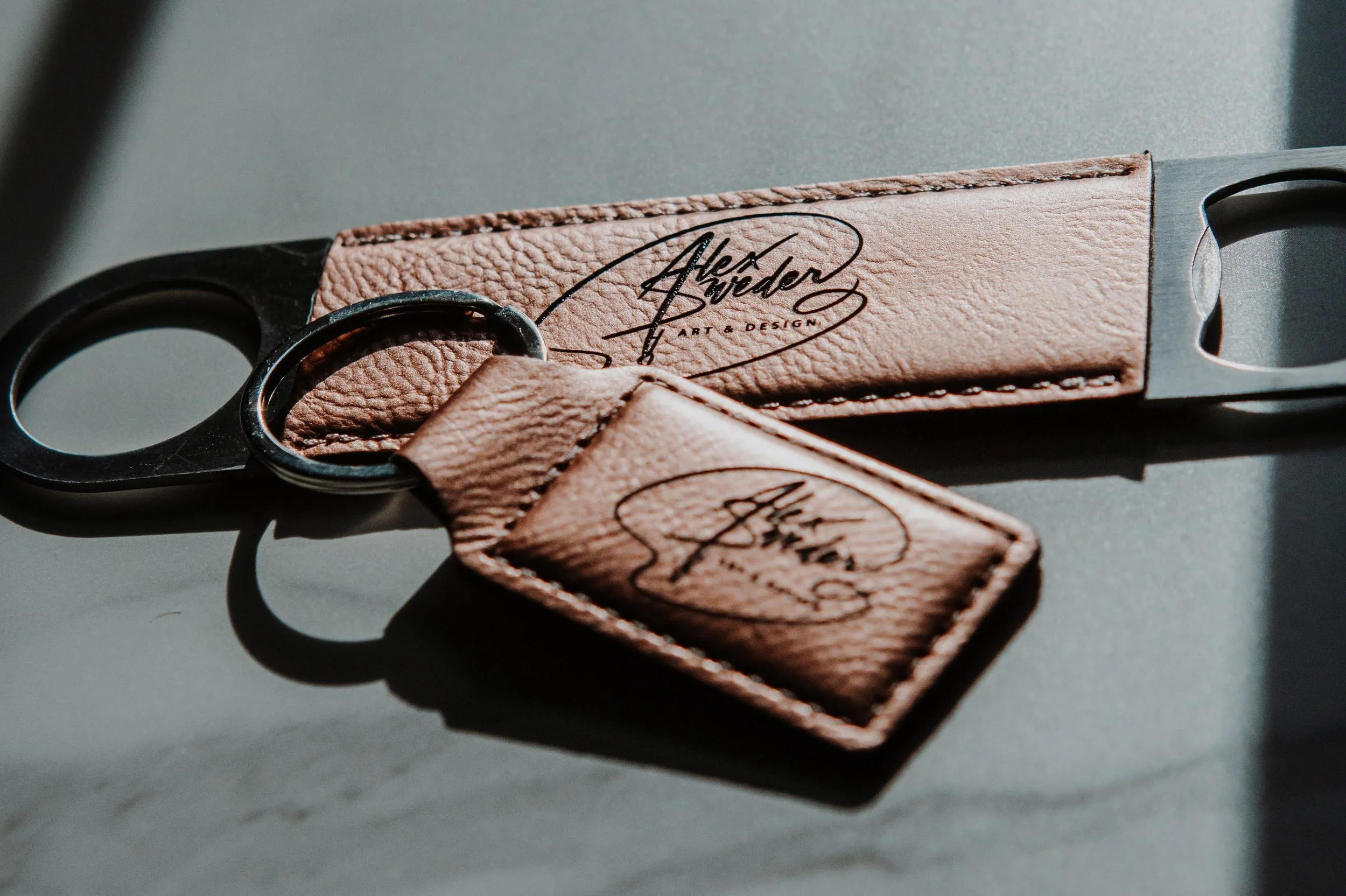 Leather keychain with a signature and text, placed on a gray surface with shadows.
