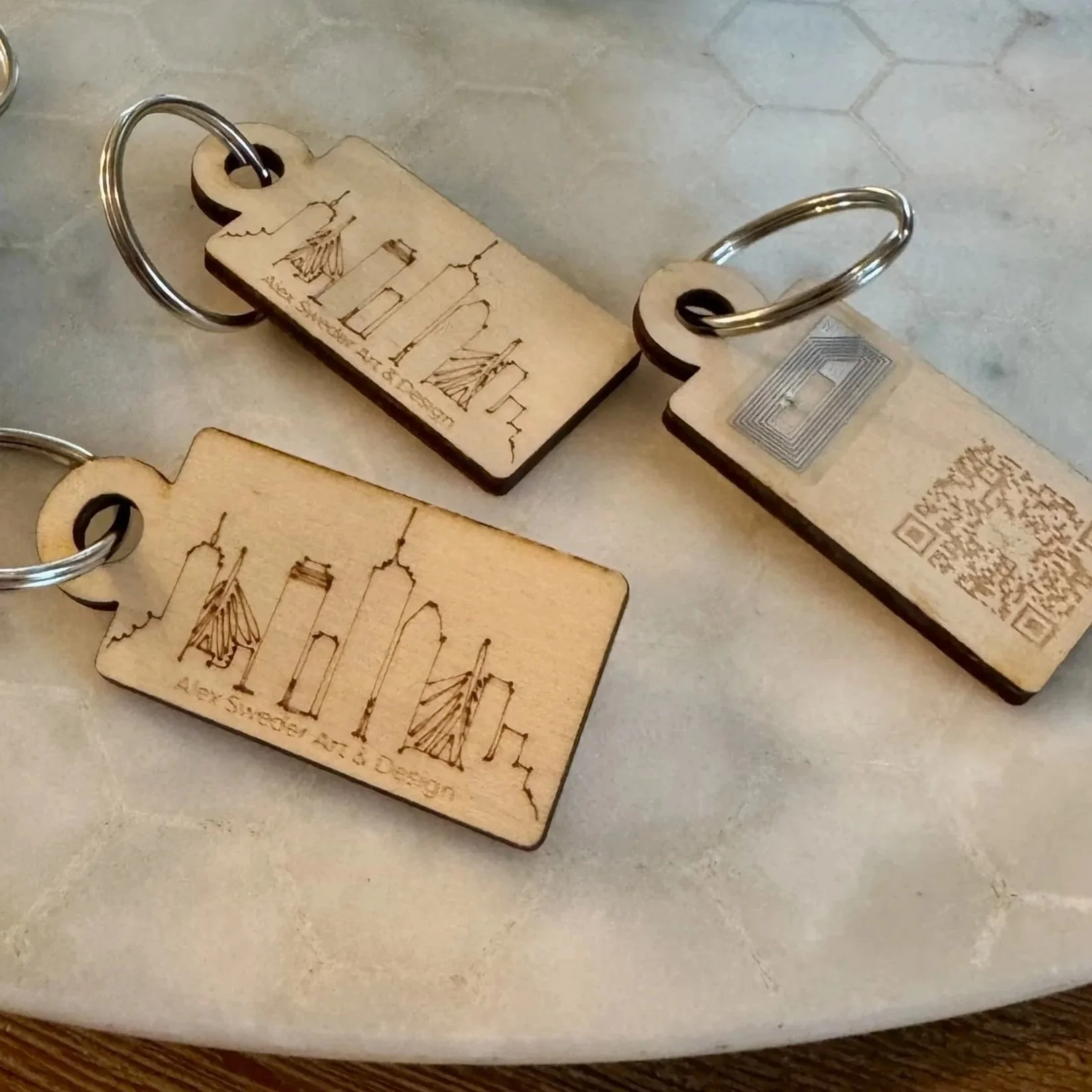 Two wooden keychains with engraved Paris city skyline and the text 'Alex Sigler M. to Design,' resting on a light-colored surface.